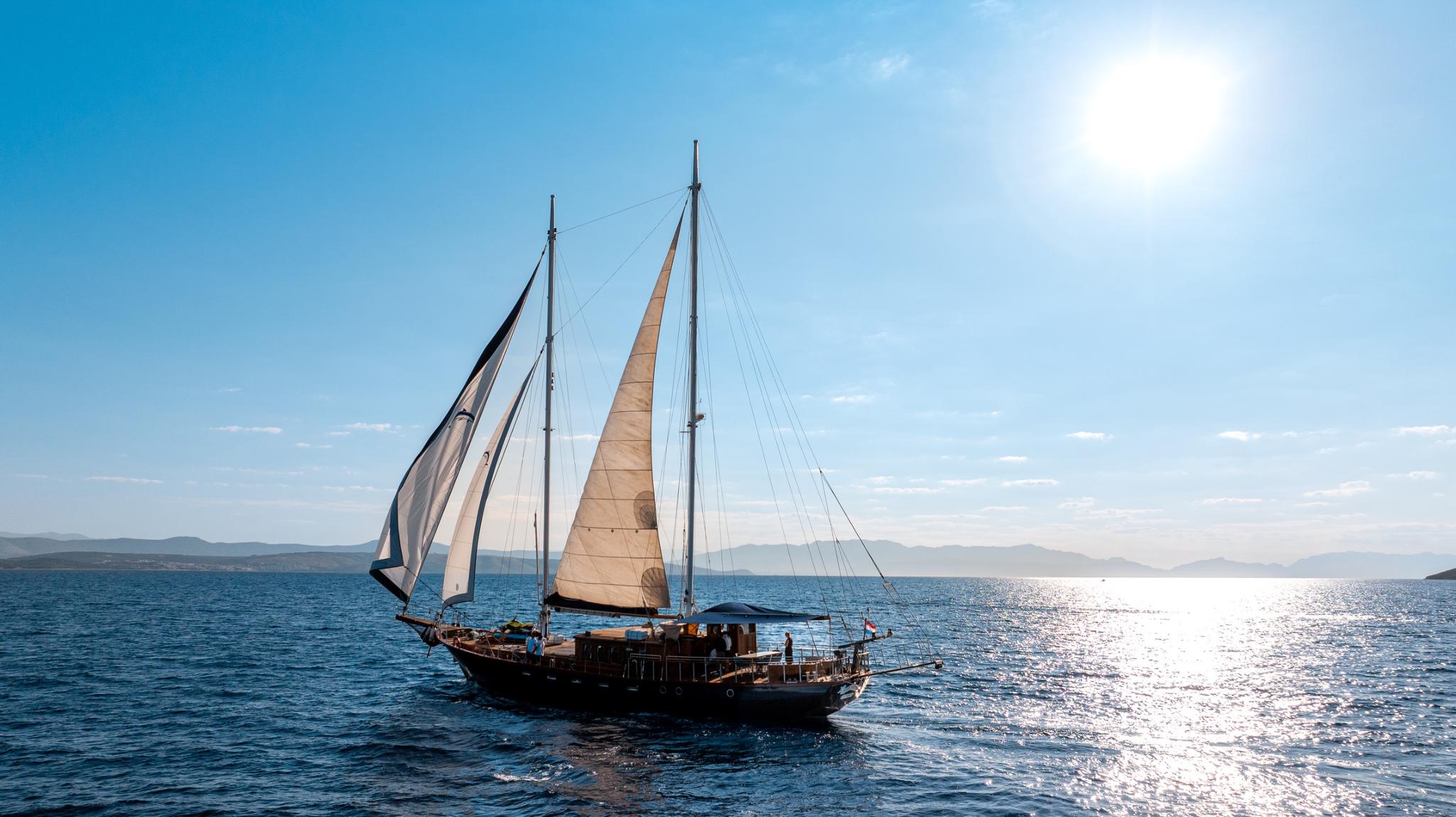 traditional wooden gulet under sail with cream colored sails on blue Mediterranean waters