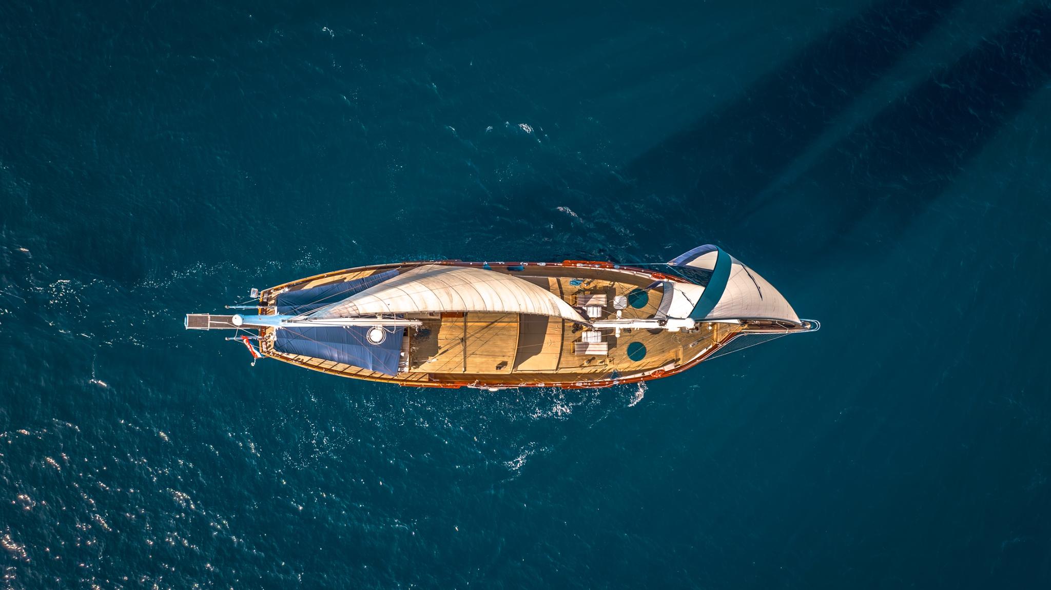 aerial view of traditional wooden gulet yacht with blue awnings sailing on turquoise water