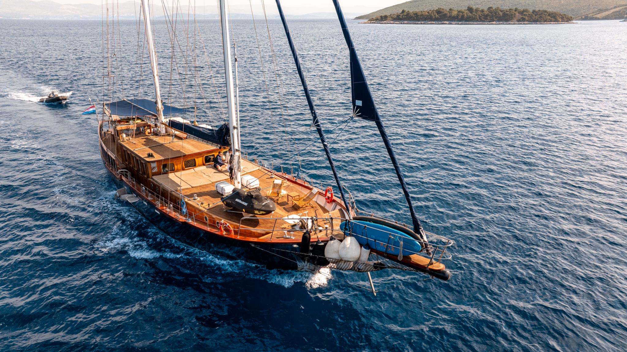 aerial drone shot of wooden gulet yacht anchored in crystal blue Mediterranean waters near coastline