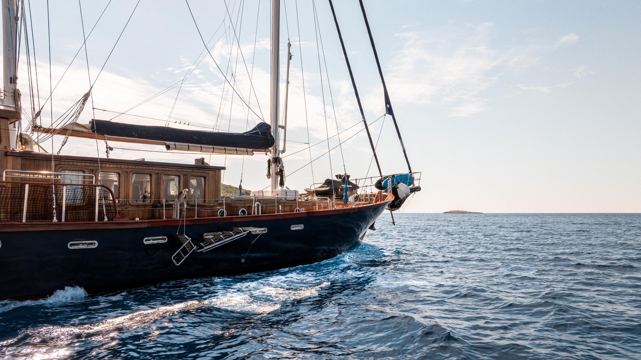 Traditional wooden gulet with dark blue hull sailing on open water with visible wake