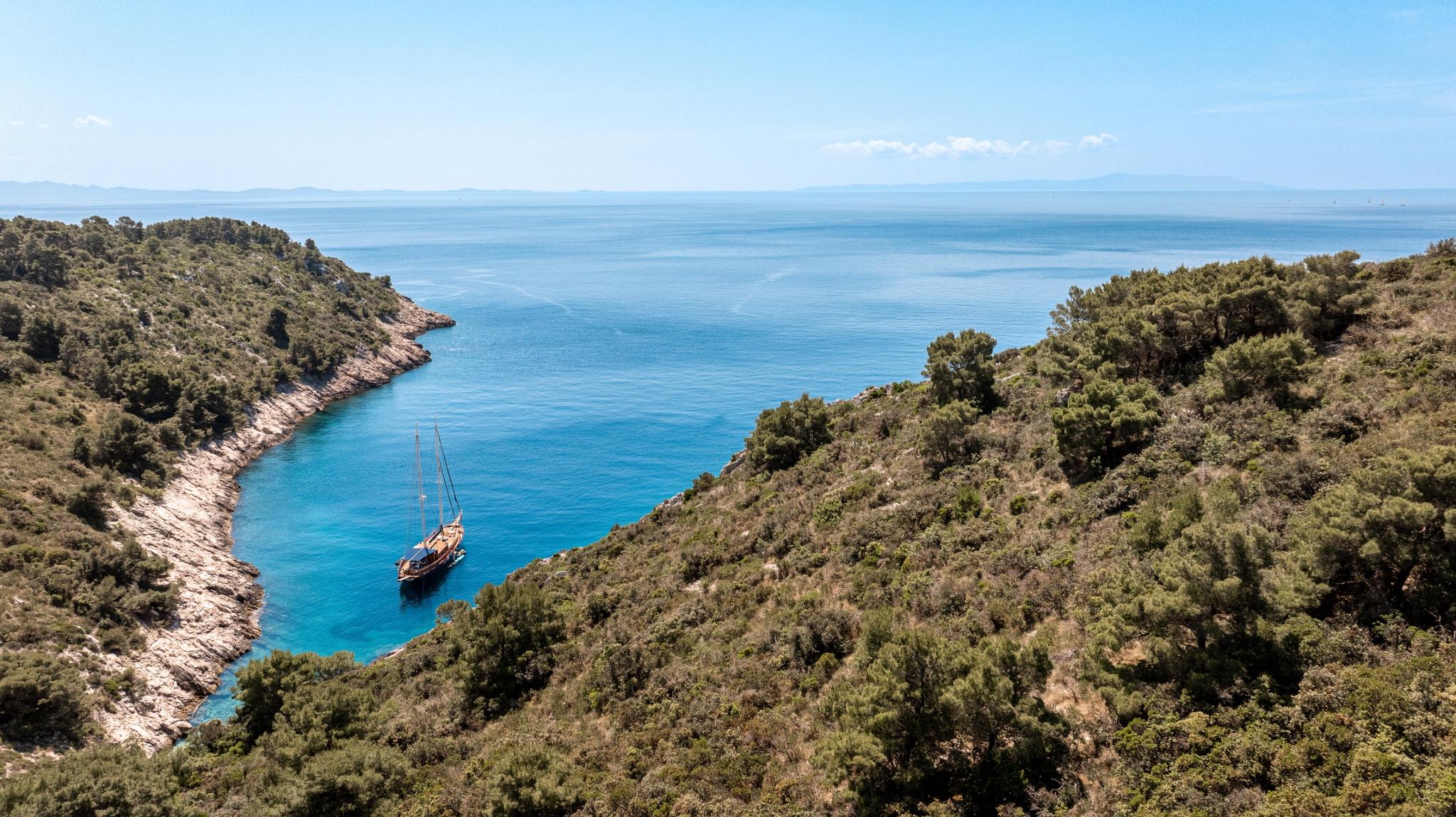 aerial view of traditional wooden gulet anchored in turquoise Mediterranean bay surrounded by pine forest
