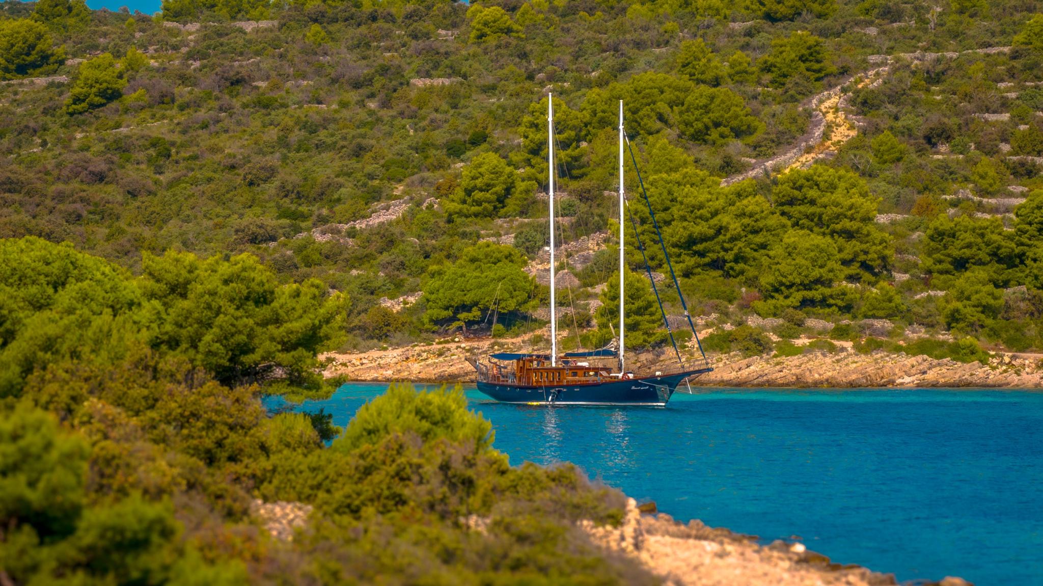 aerial view of traditional wooden gulet yacht anchored in turquoise bay surrounded by pine forest