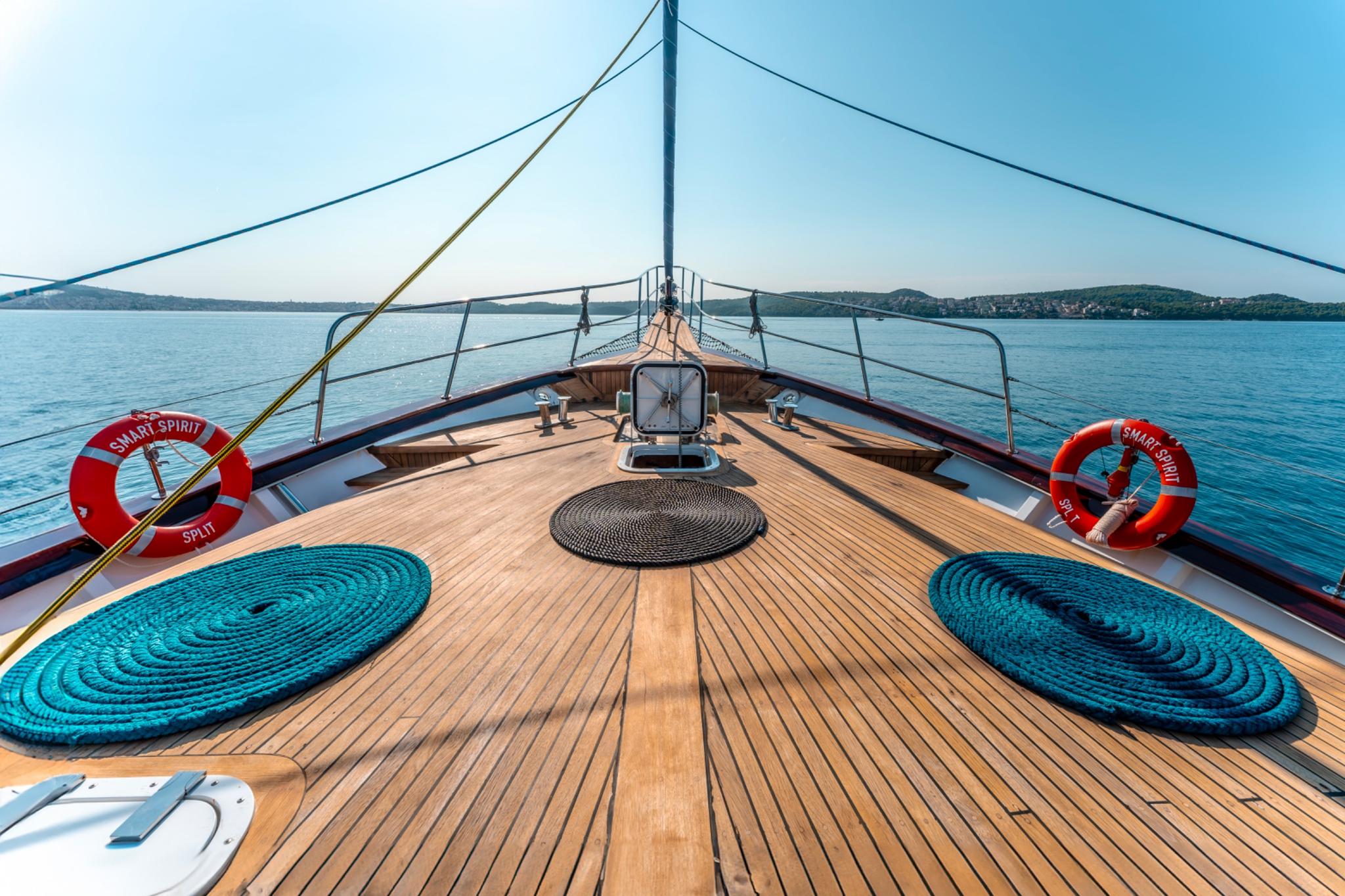 Gulet bow deck with teak planking, coiled blue and black ropes, life rings, and stainless steel railings