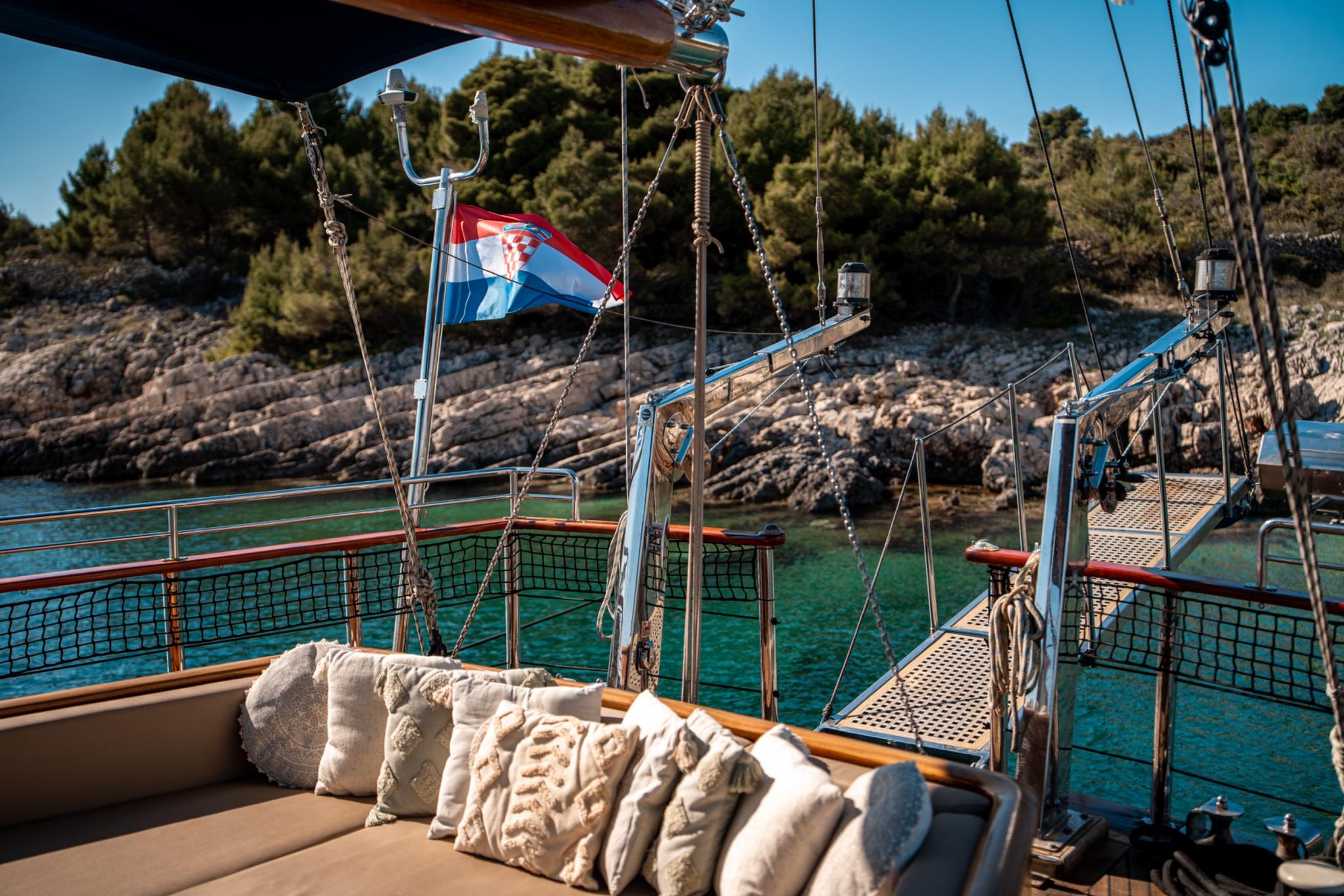 gulet aft deck with beige cushioned seating area and Croatian flag flying