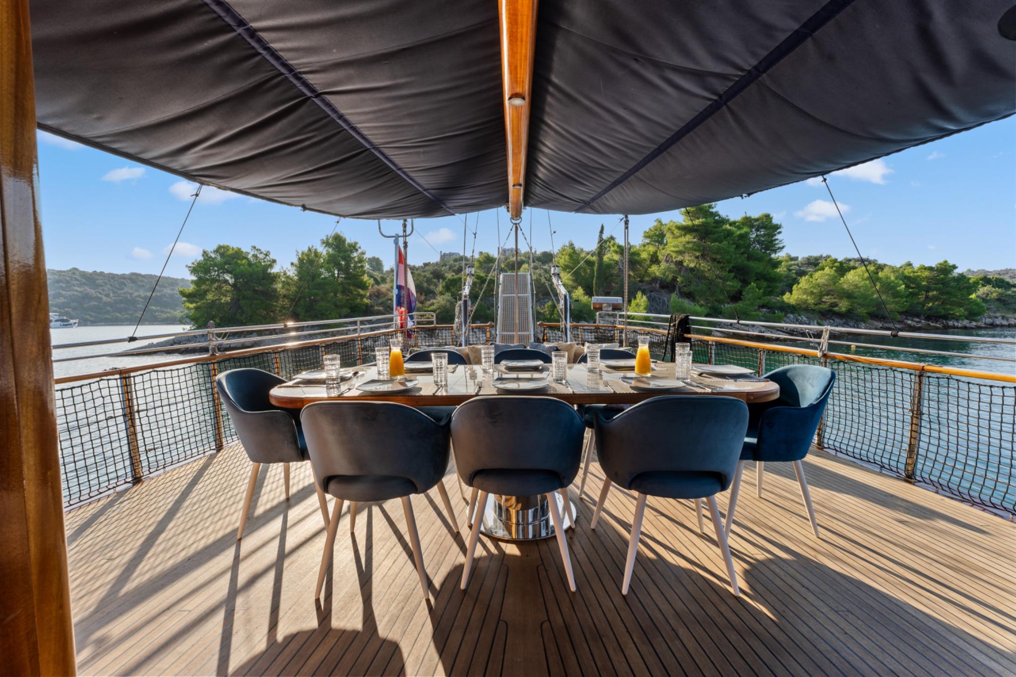 aft deck dining table with modern chairs under awning overlooking forested coastline