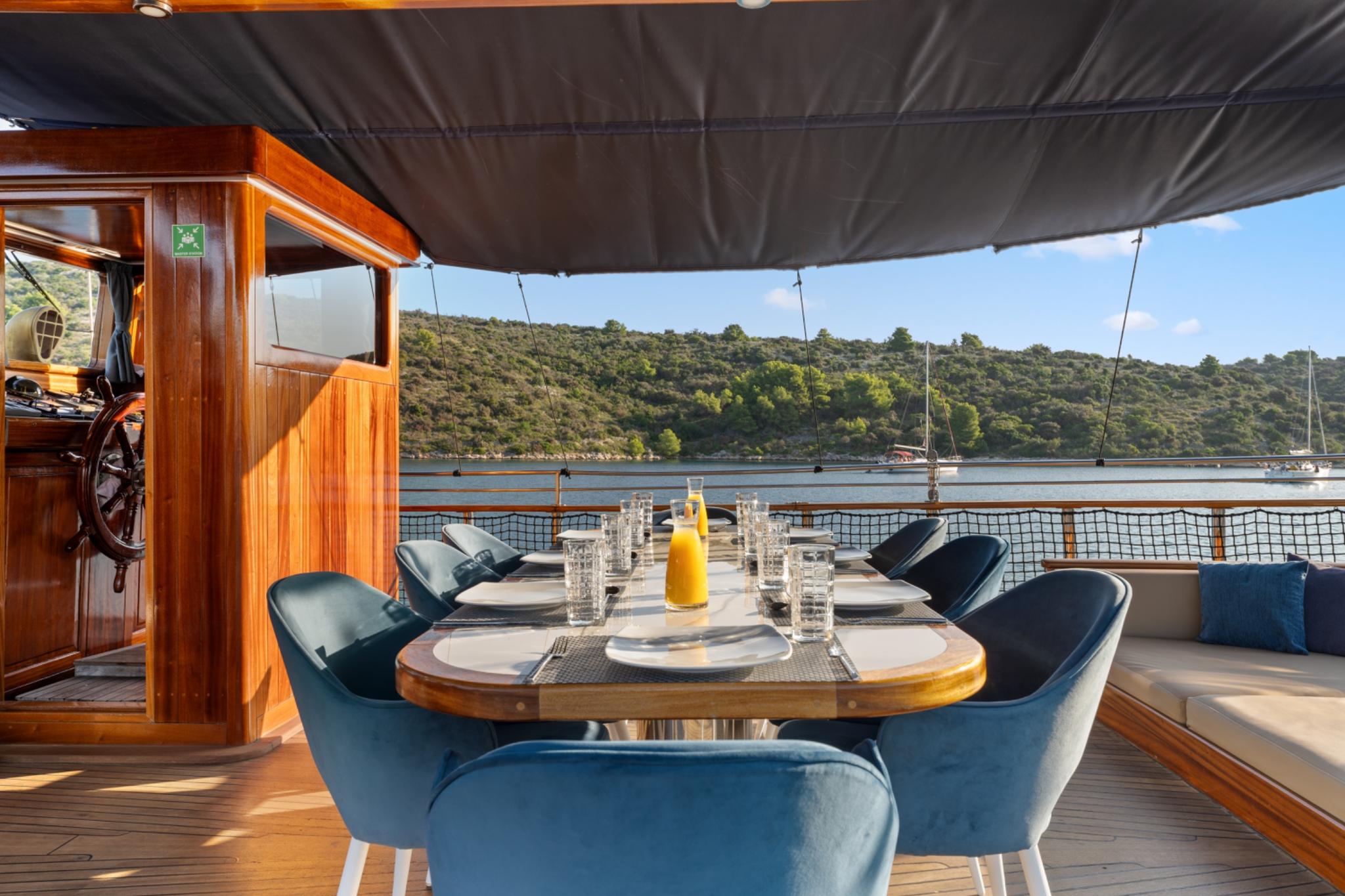 covered aft deck dining table with blue upholstered chairs and coastal view