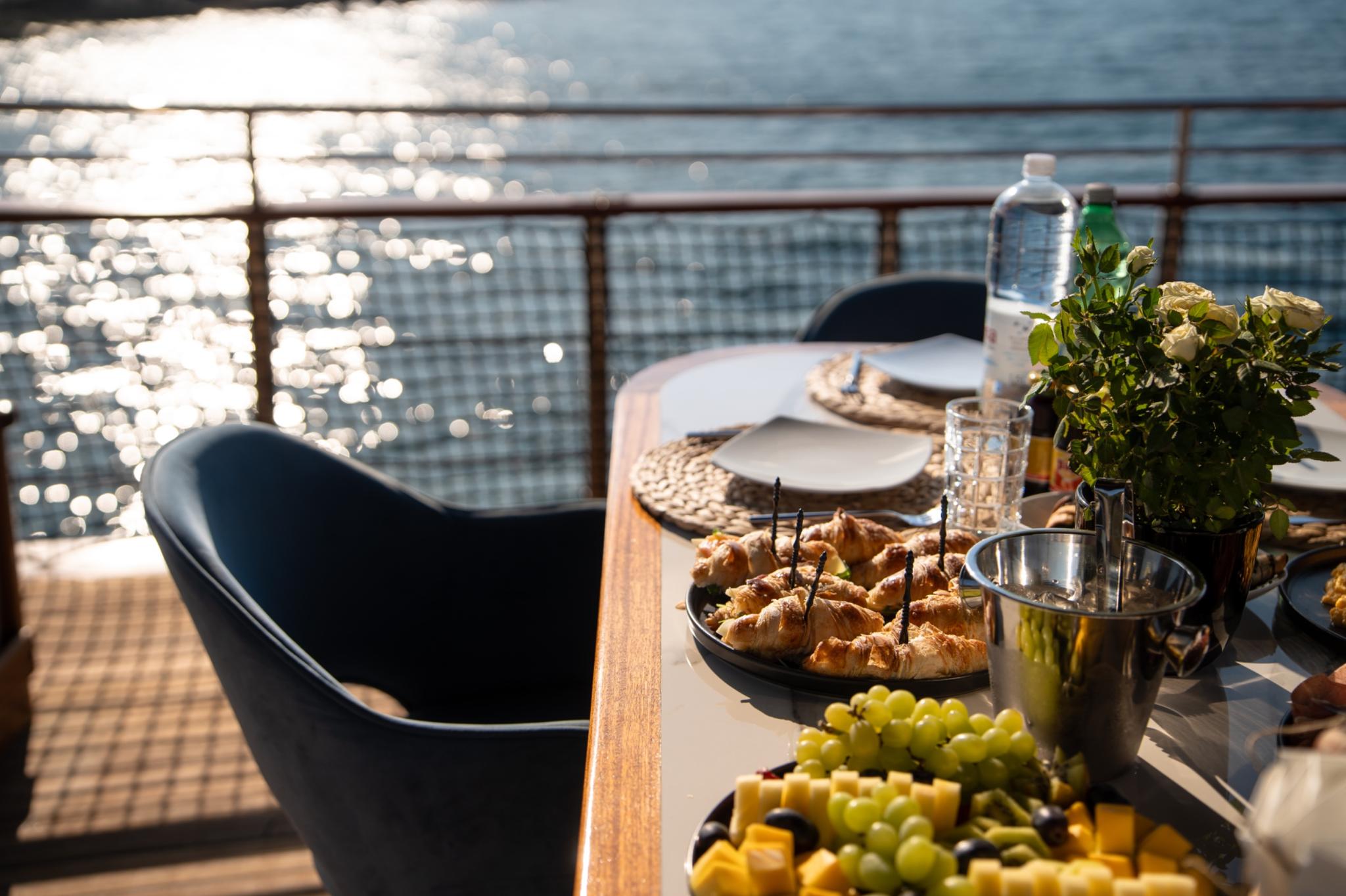 yacht deck dining table with pastries, cheese platter, grapes and beverages served