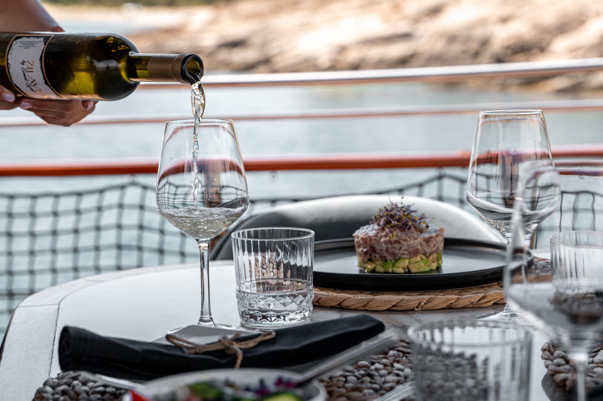 white wine being poured into glass with gourmet plated dish on yacht dining table