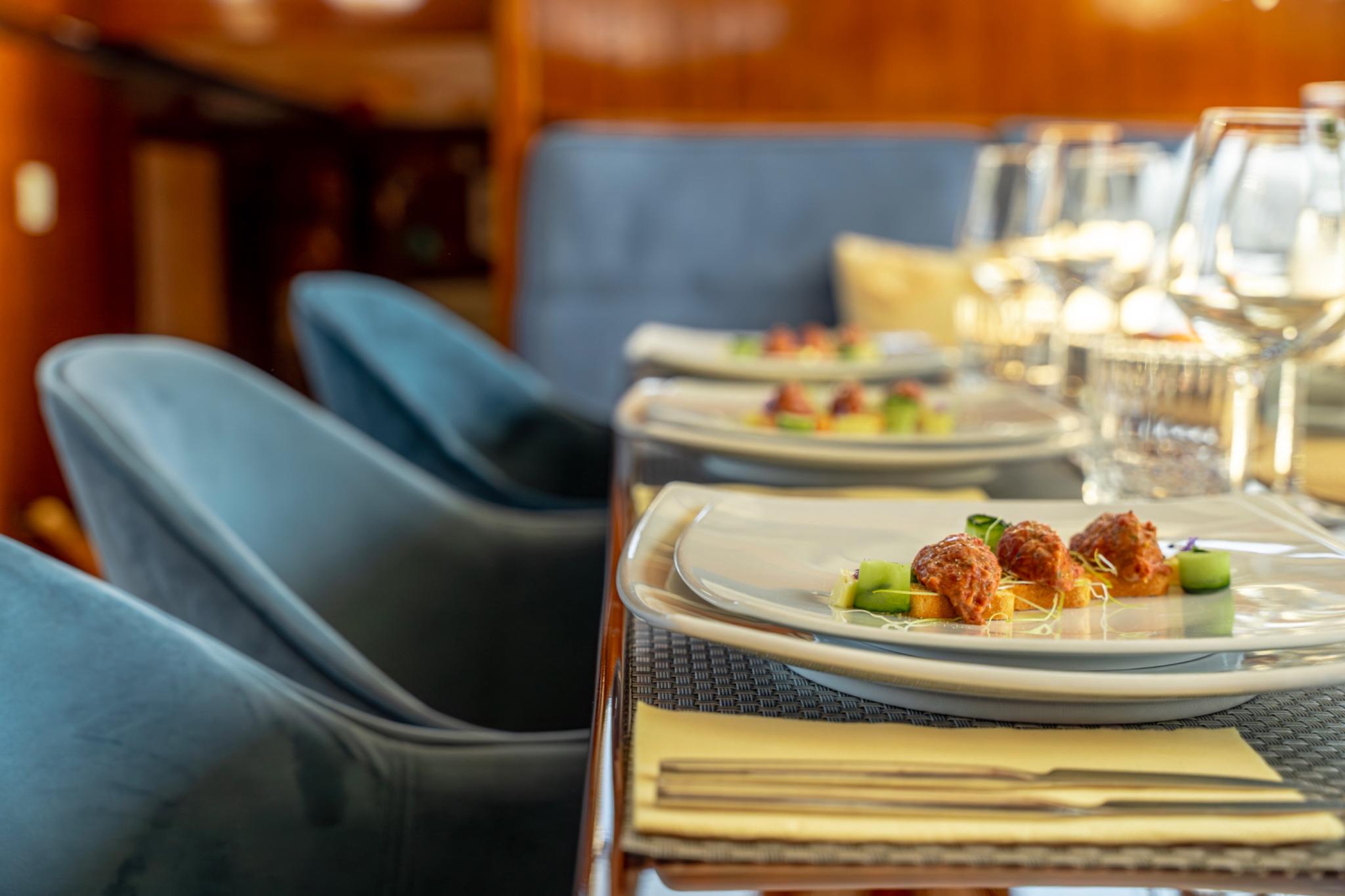 luxury yacht dining table with gourmet appetizers, wine glasses and blue upholstered chairs
