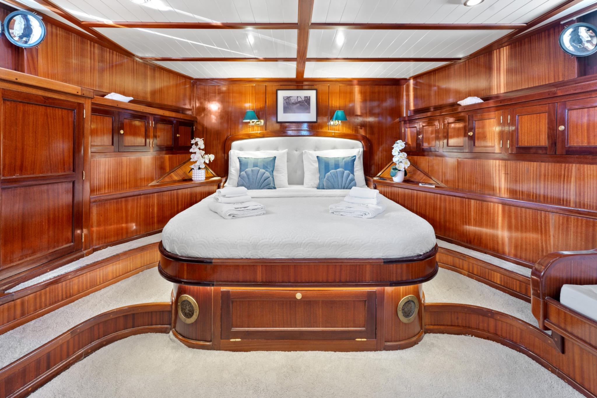 luxurious master cabin featuring king bed, rich wood paneling, built-in storage and nautical portholes