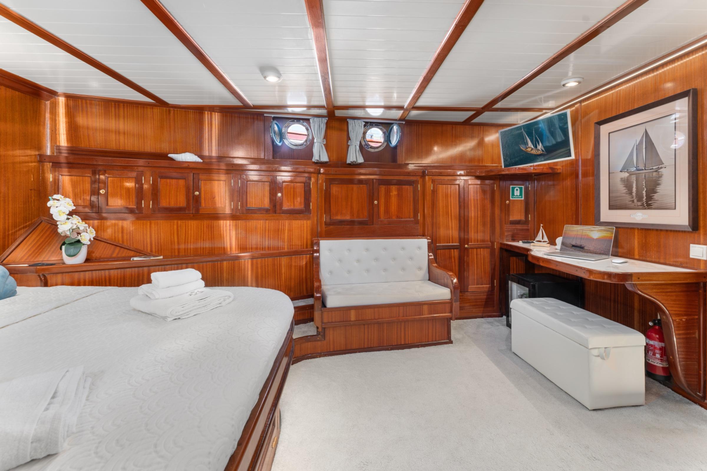yacht cabin interior with double bed, built-in seating, wooden paneling and portholes