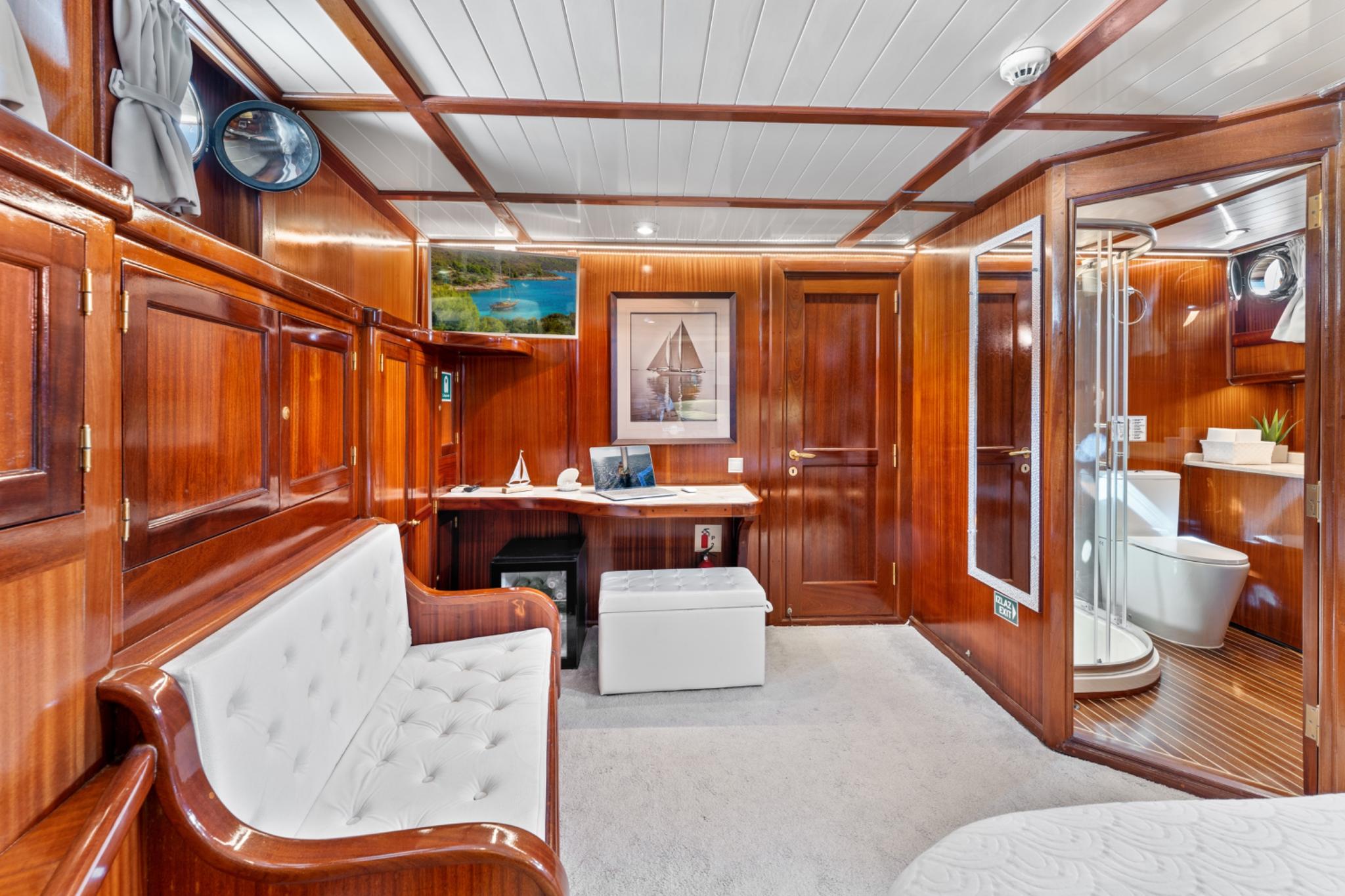 luxury yacht master cabin with built-in desk, tufted seating and glass-enclosed ensuite bathroom