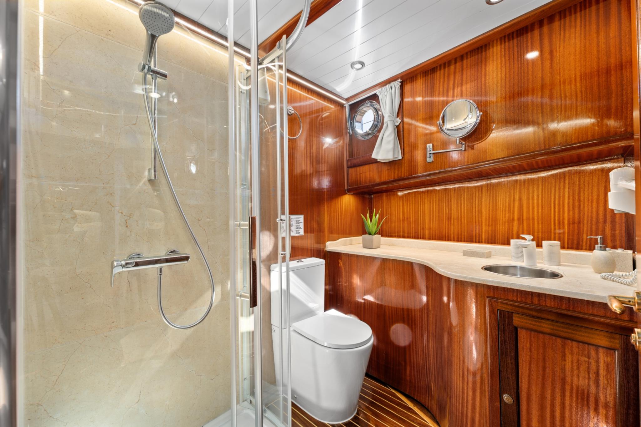 yacht bathroom featuring glass shower enclosure, toilet, marble vanity counter with wooden cabinetry