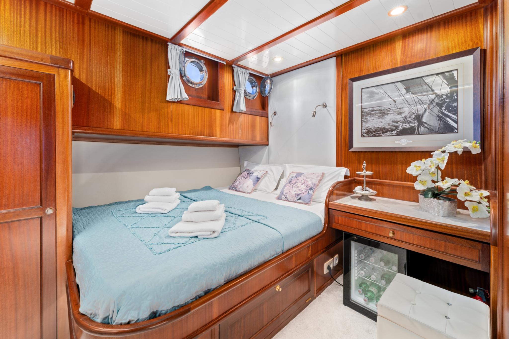 yacht guest cabin with double bed, wood paneling, portholes and maritime artwork
