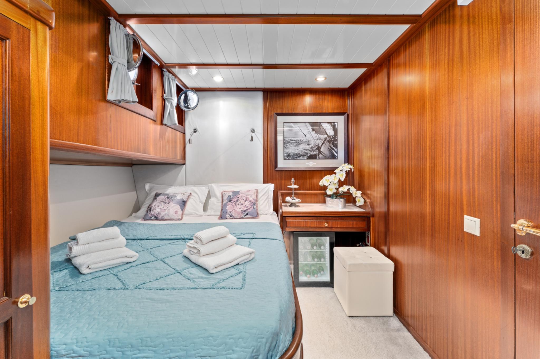 yacht guest cabin featuring double bed with teal bedding, wood paneling, and built-in mini fridge