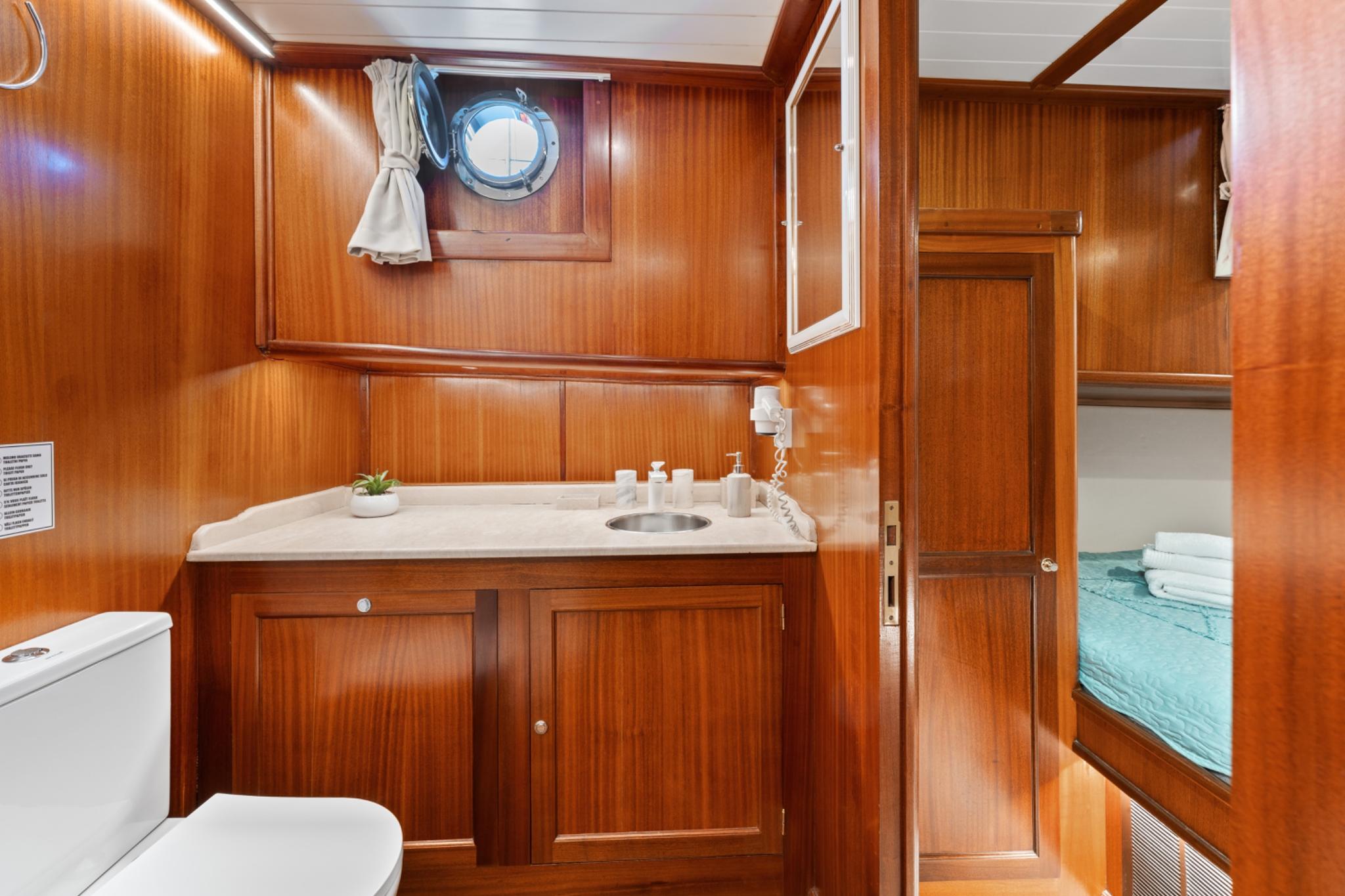 yacht cabin en-suite bathroom featuring teak vanity unit with marble countertop and circular porthole