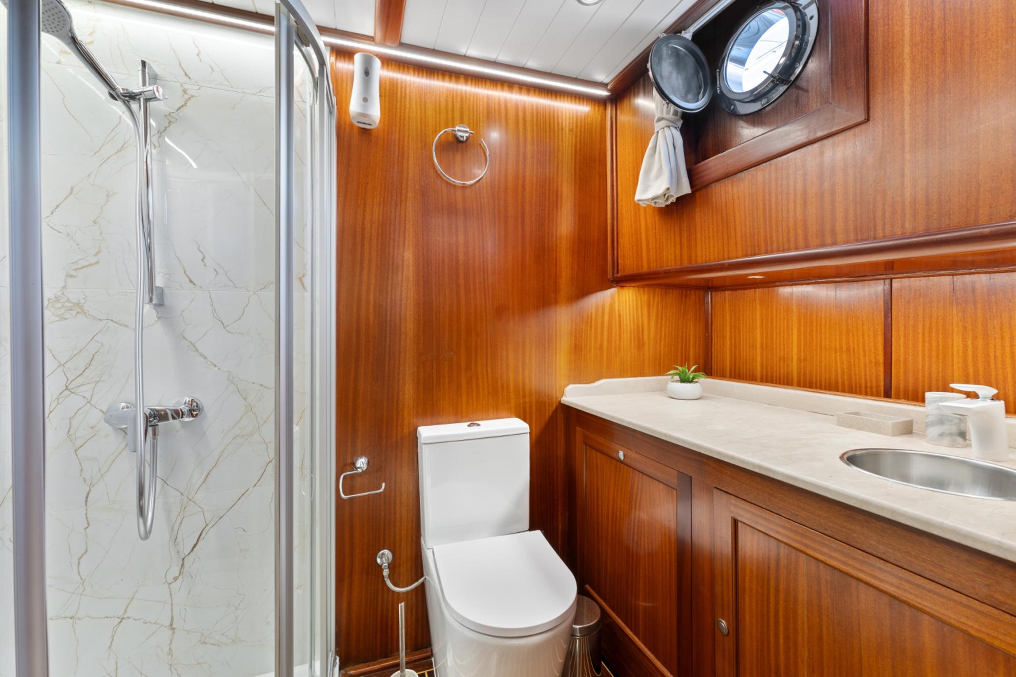 yacht bathroom featuring marble shower, toilet, wooden vanity with sink and two portholes