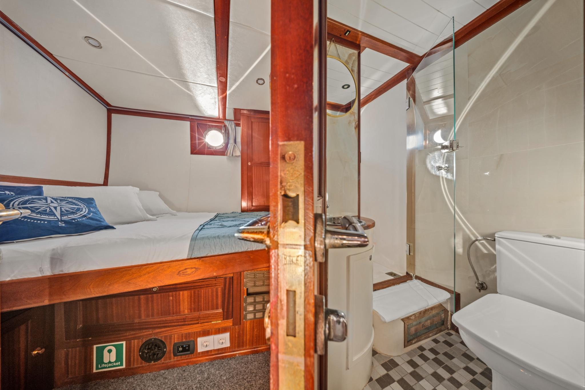 yacht cabin interior showing bed with nautical bedding and adjacent en-suite bathroom with toilet