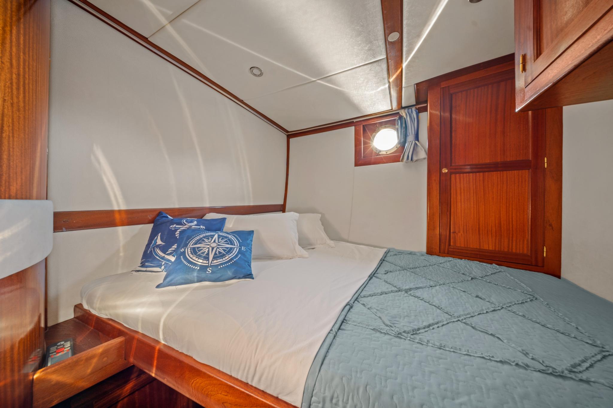yacht guest cabin featuring double bed with compass-themed pillows and teal throw