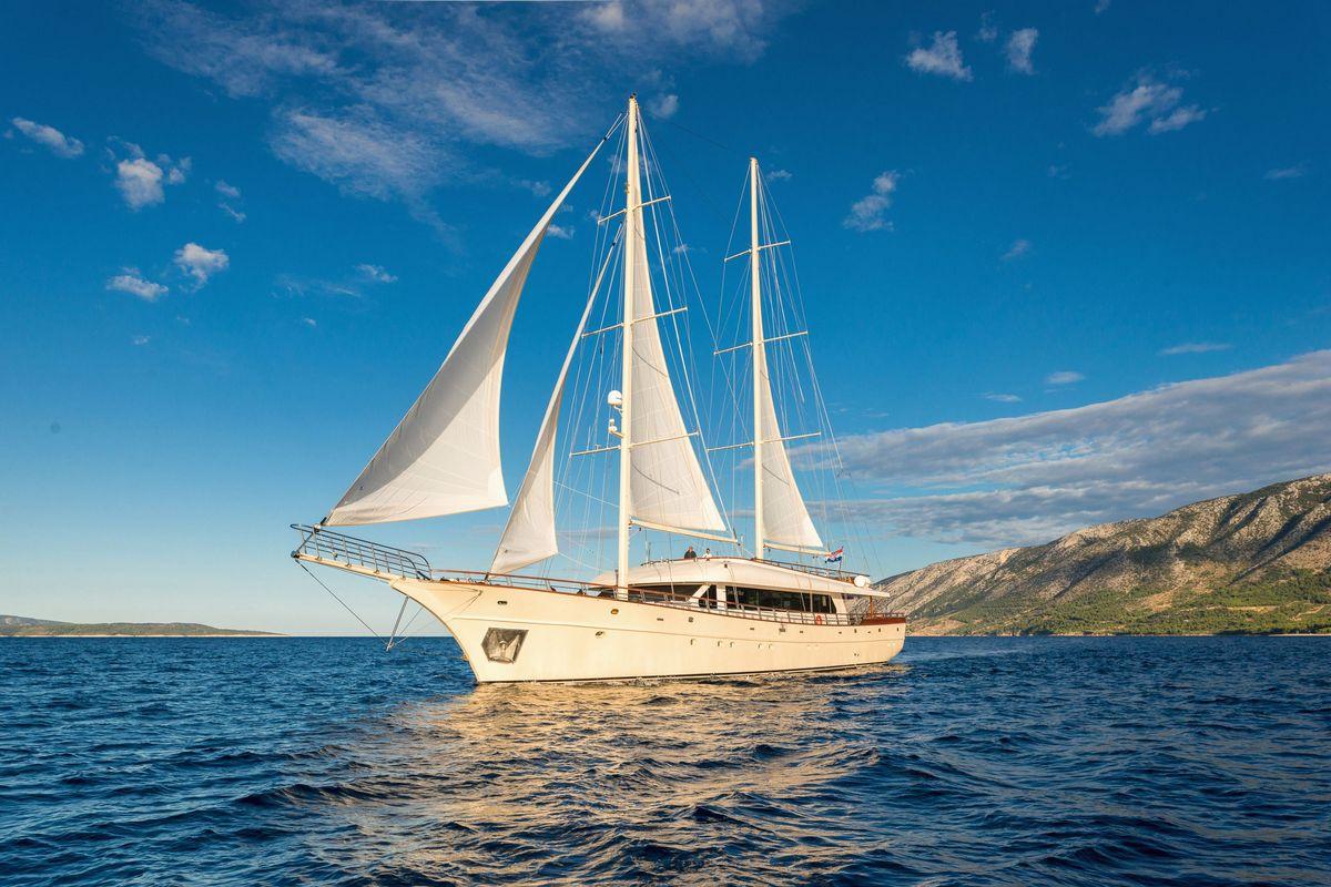 Traditional white gulet yacht sailing with full sails against mountainous coastline