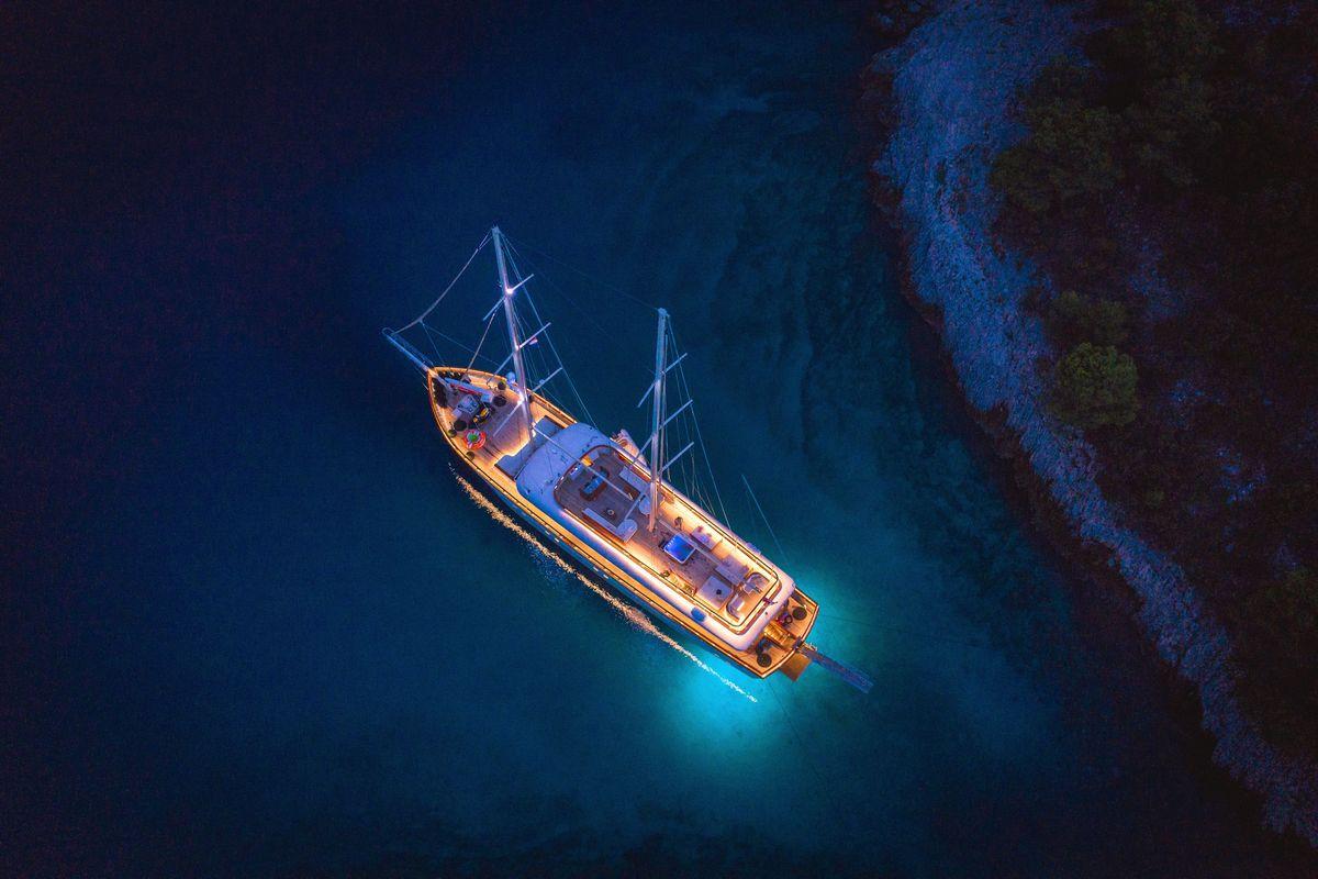 aerial night view of illuminated wooden gulet yacht in turquoise waters