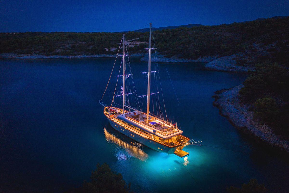 Luxury sailing yacht with golden deck lighting anchored in Mediterranean bay at twilight