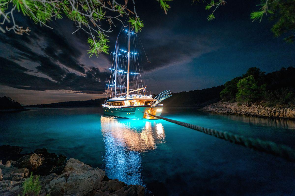 luxury sailing yacht with blue underwater lighting anchored in turquoise cove at night