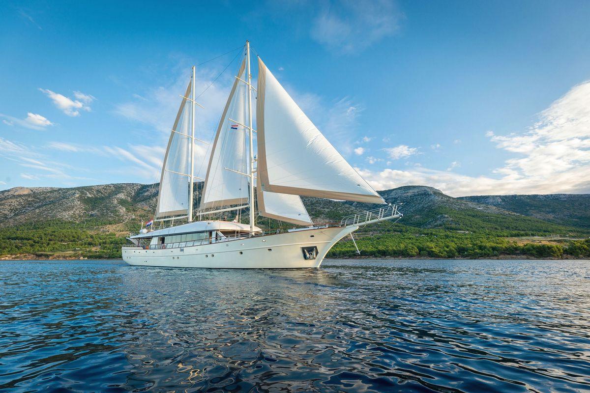 White sailing gulet yacht with two masts and sails near forested coastline