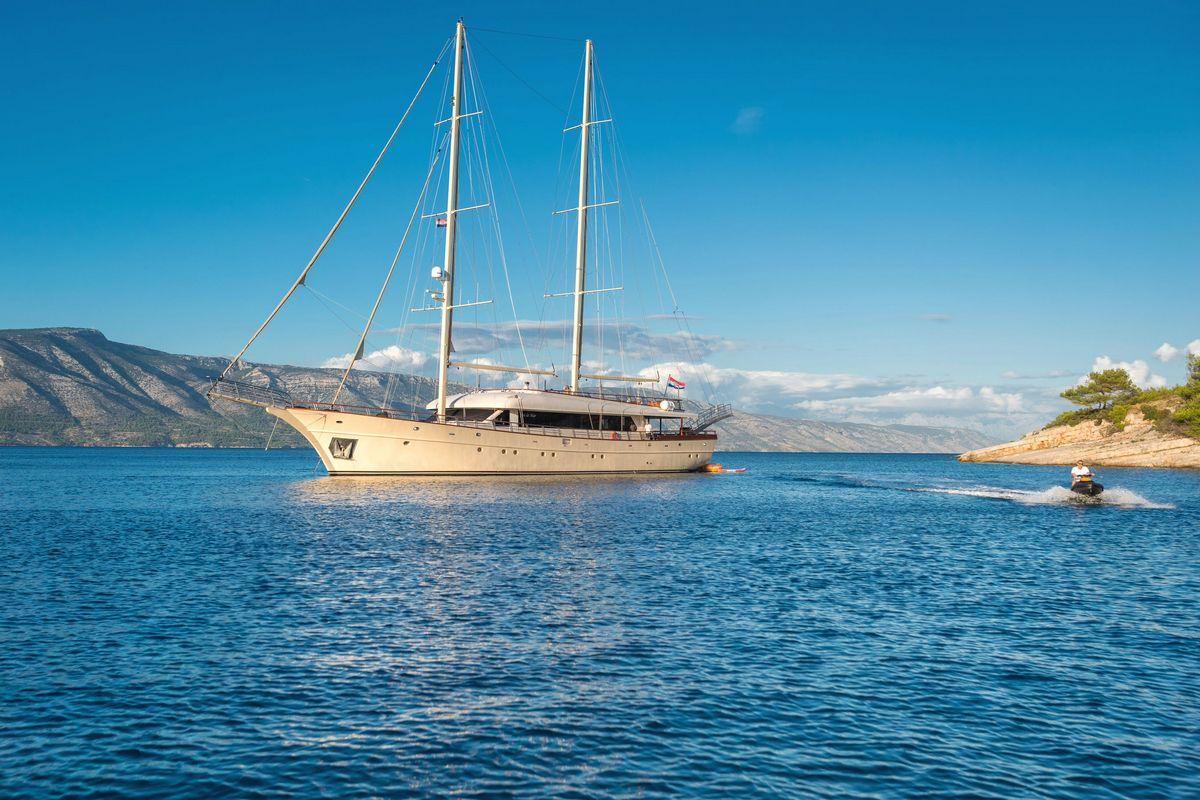 White luxury motor yacht with twin masts anchored in blue Mediterranean bay
