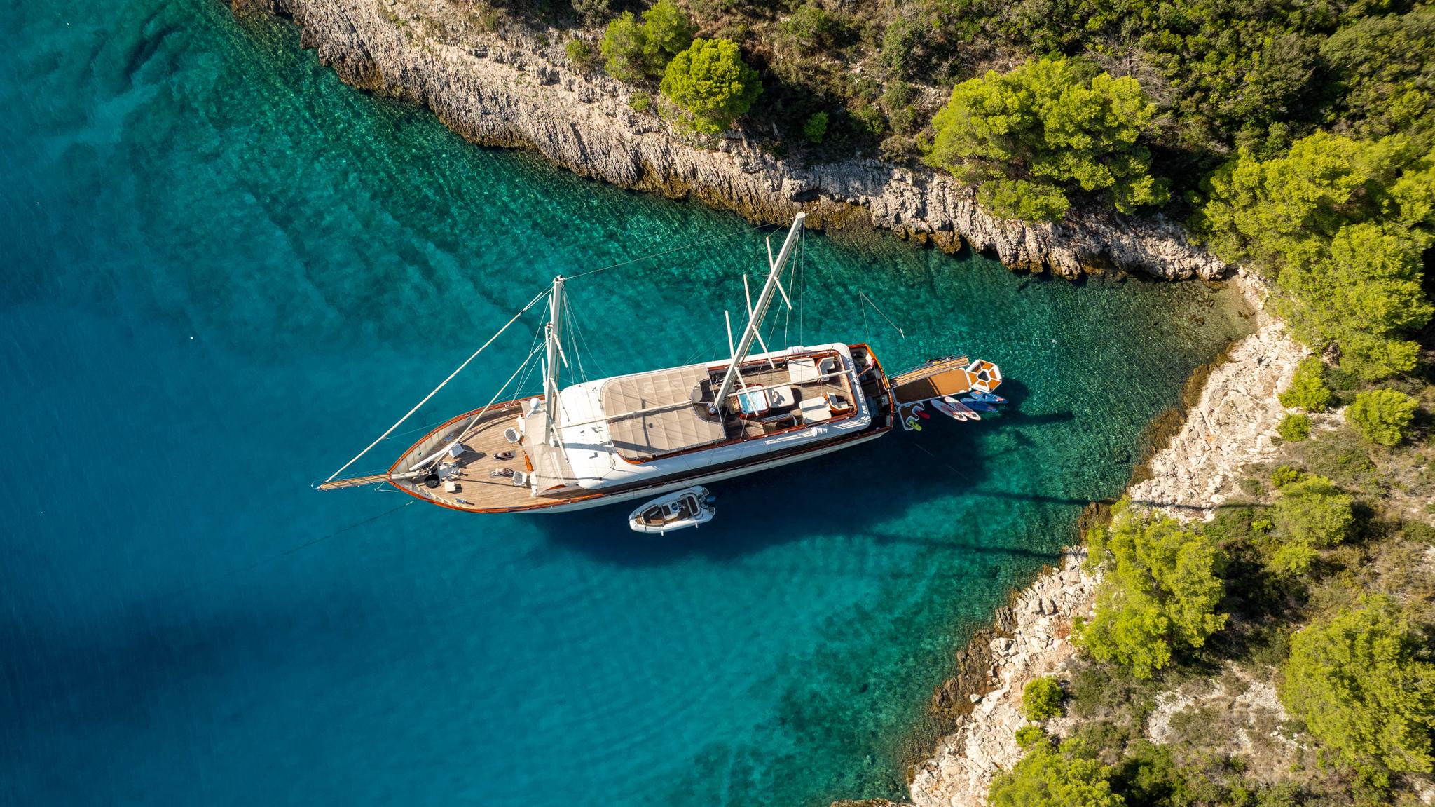 aerial view of luxury gulet yacht anchored in crystal clear turquoise bay with rocky coastline