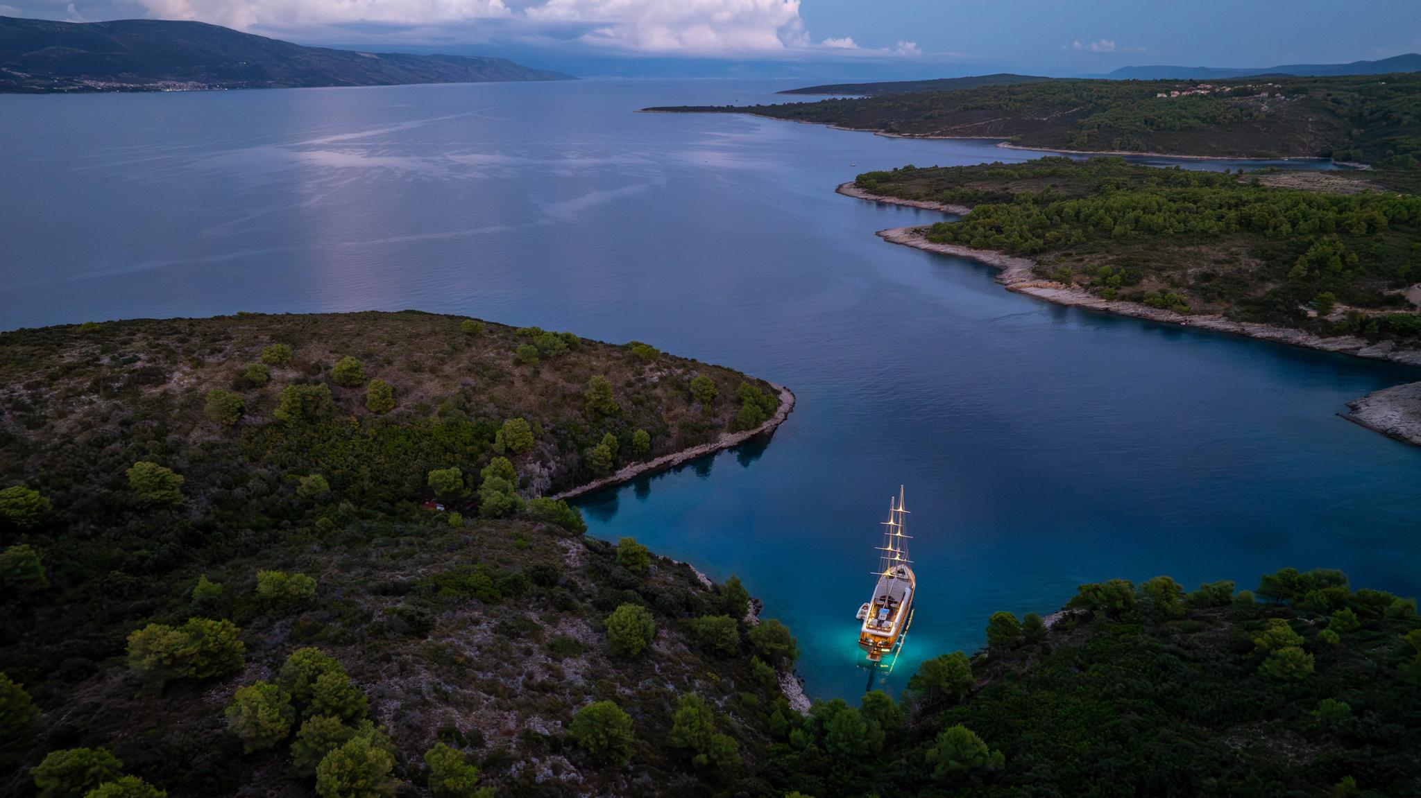 Aerial view of wooden gulet yacht anchored in turquoise bay surrounded by forested coastline