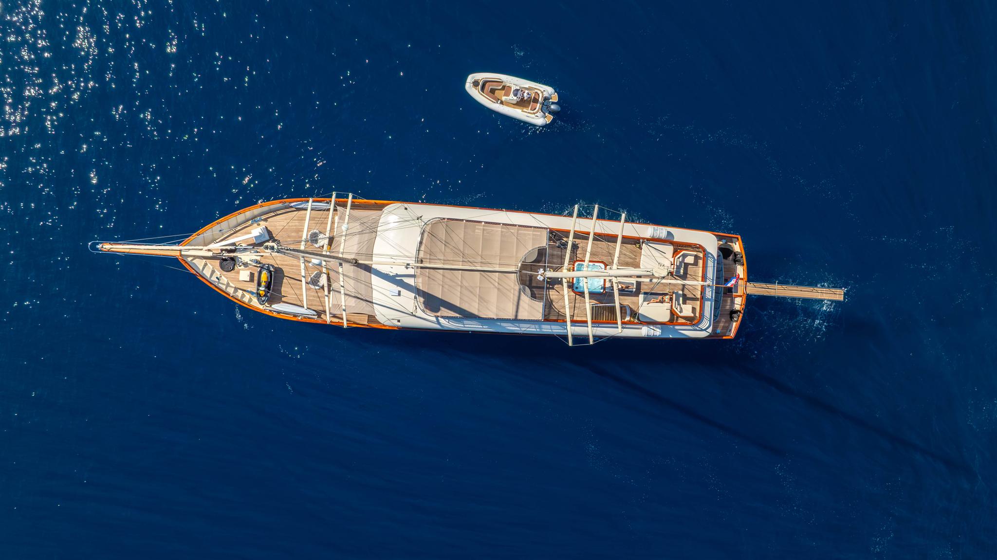 aerial drone view of traditional gulet yacht with wooden deck and white tender boat in deep blue water