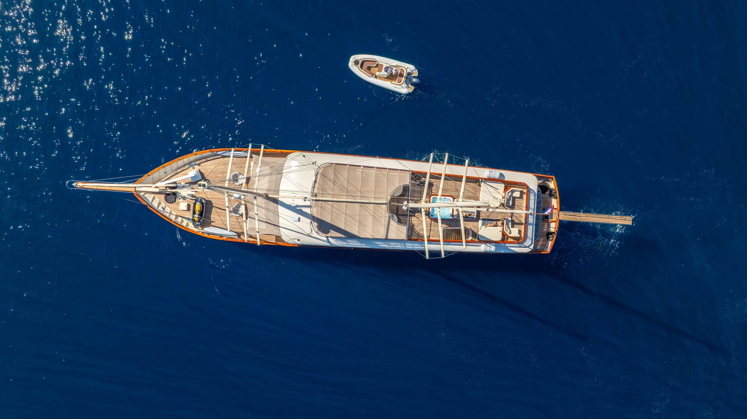 aerial drone view of traditional gulet yacht with wooden deck and white tender boat in deep blue water