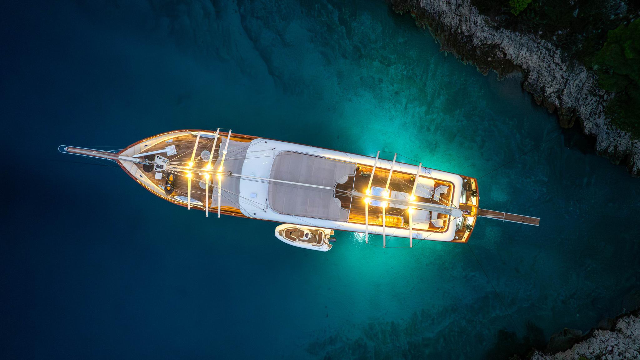 aerial view of white gulet yacht anchored in crystal clear turquoise waters with tender boat