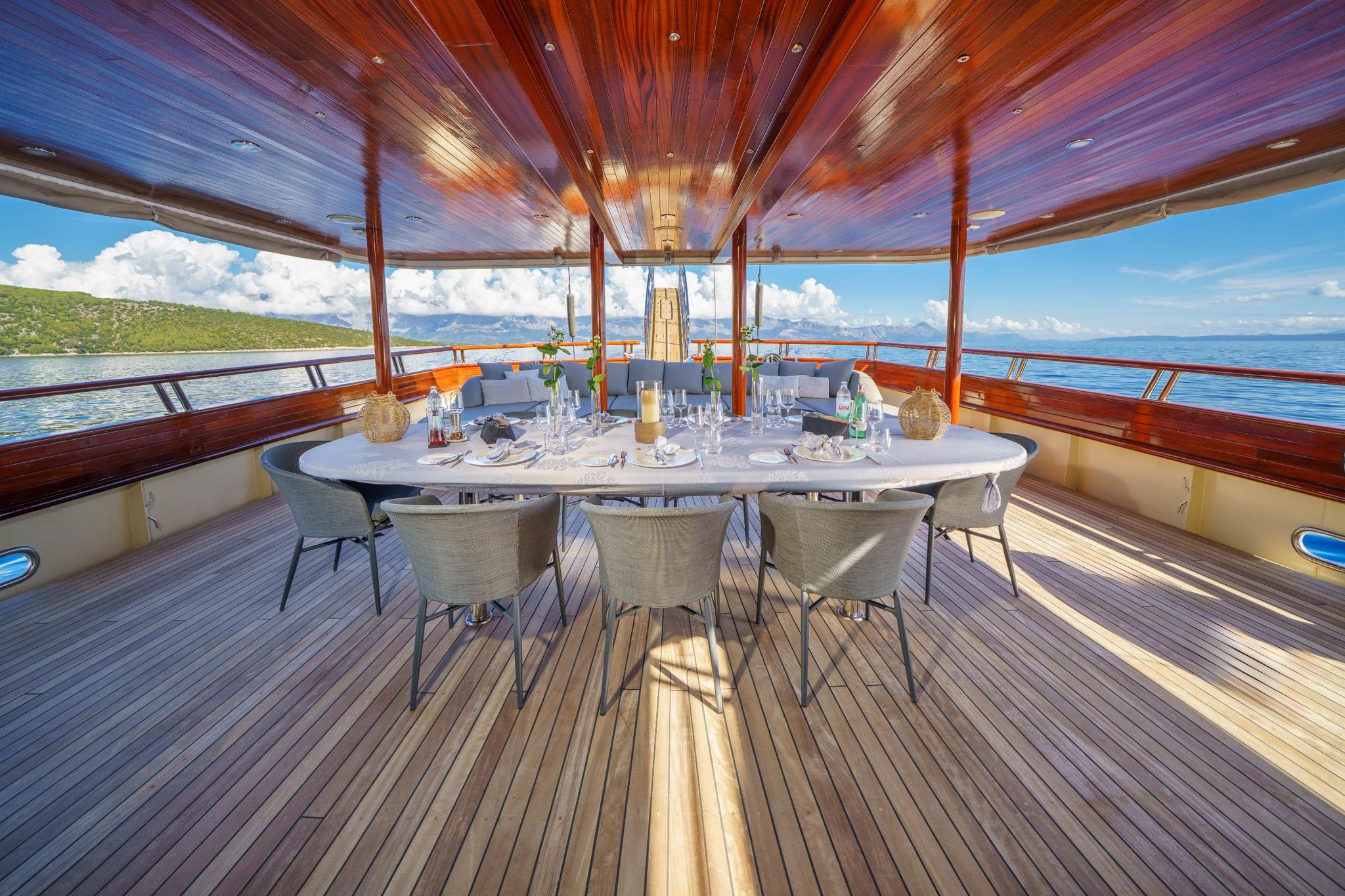 covered aft deck dining area with white oval table, wicker chairs, and wood ceiling