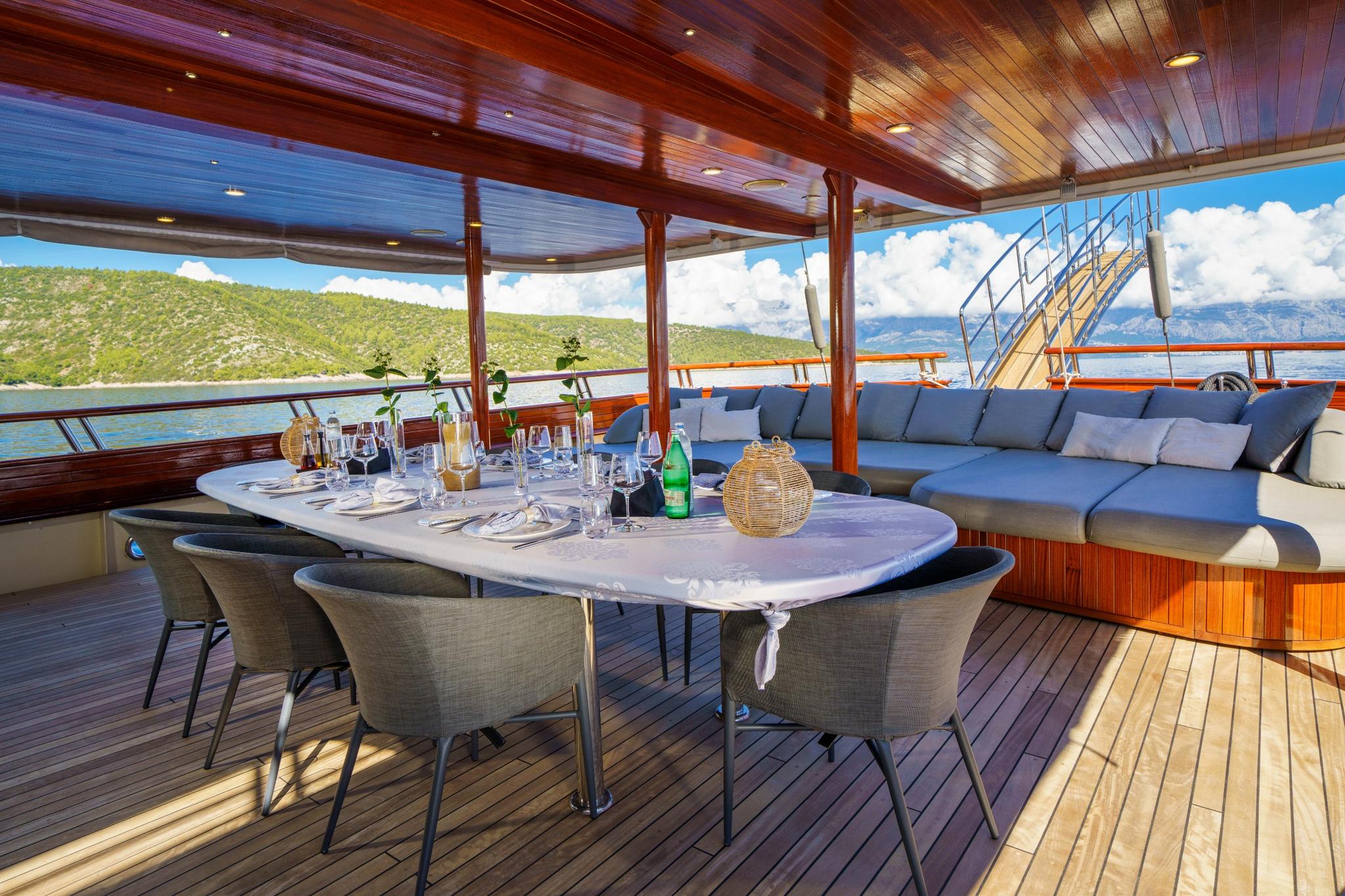 covered aft deck with dining table, wicker chairs, and blue cushioned seating area