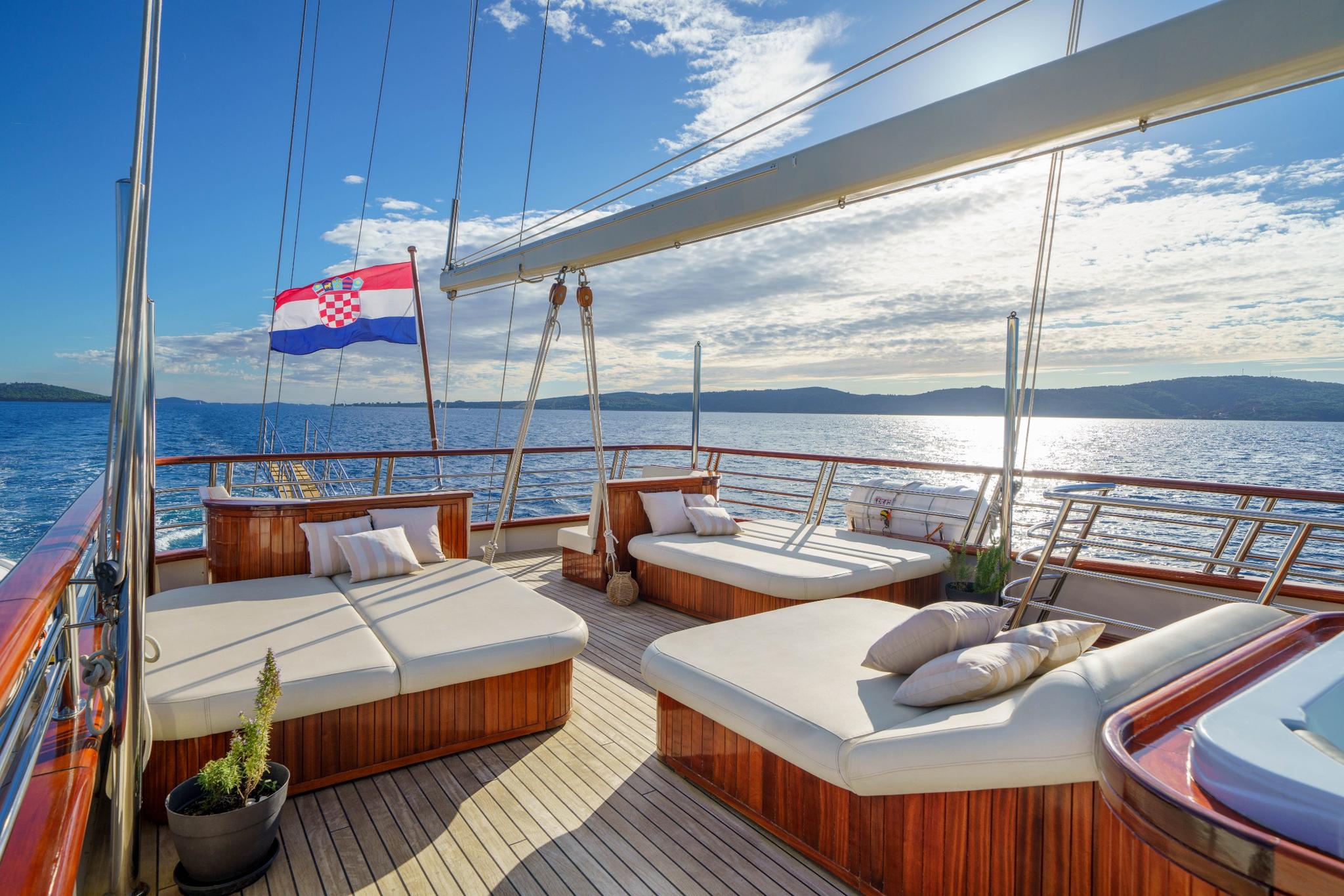 Gulet bow sun deck with teak wood cushioned loungers and Croatian flag flying