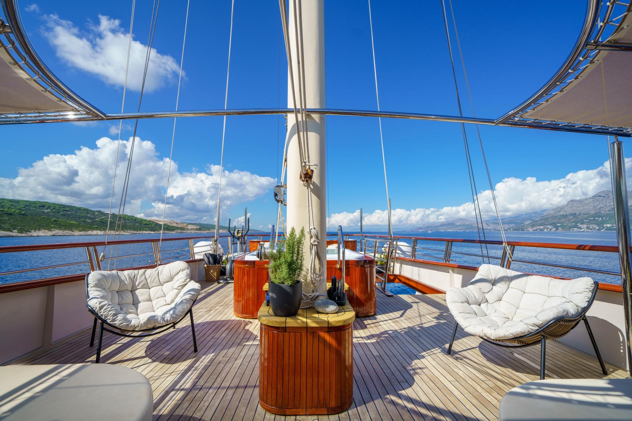 gulet forward deck with white cushioned chairs around central mast and teak decking