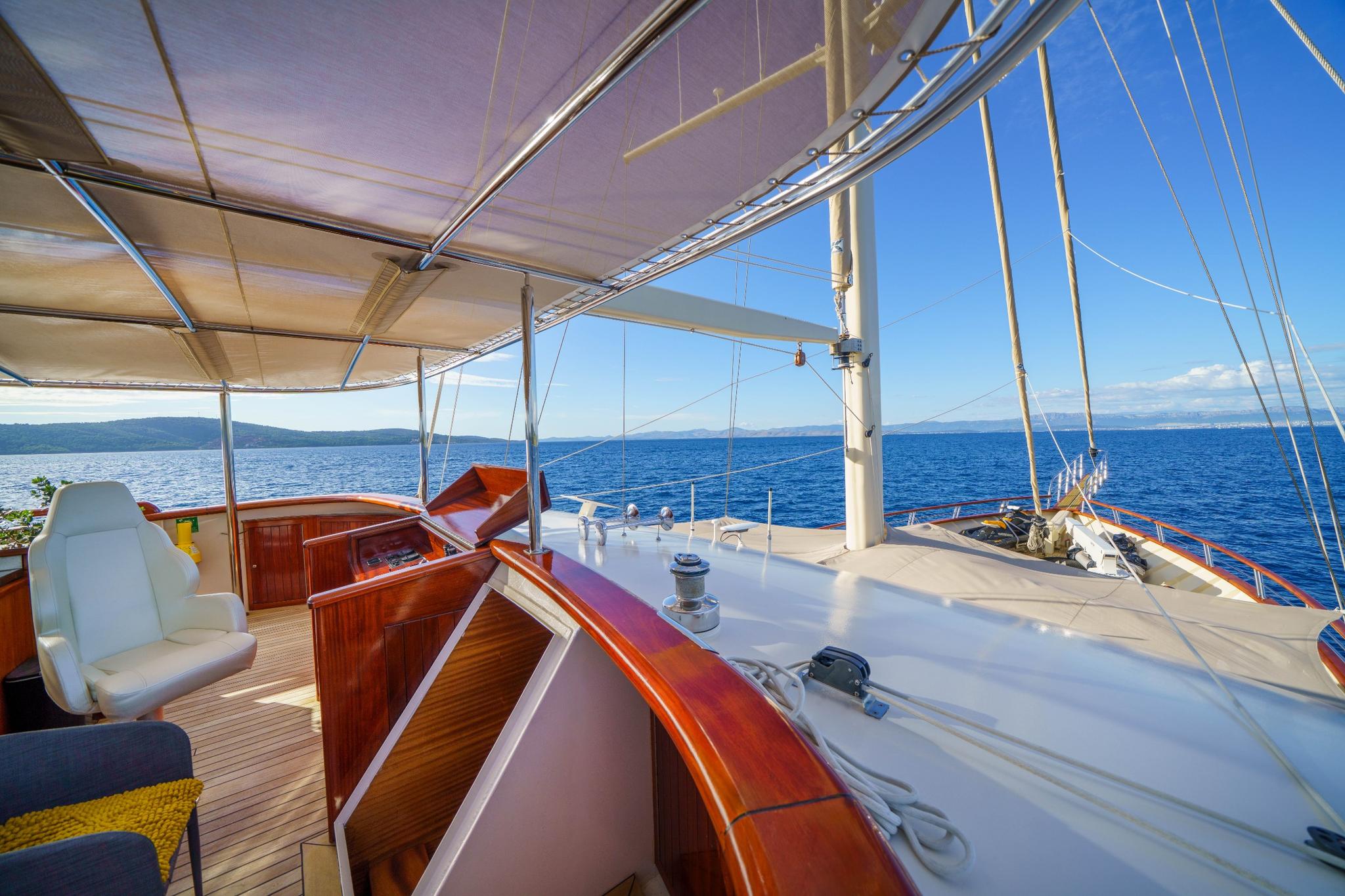 gulet helm station with white captain's chair and polished wood wheelhouse under canvas awning