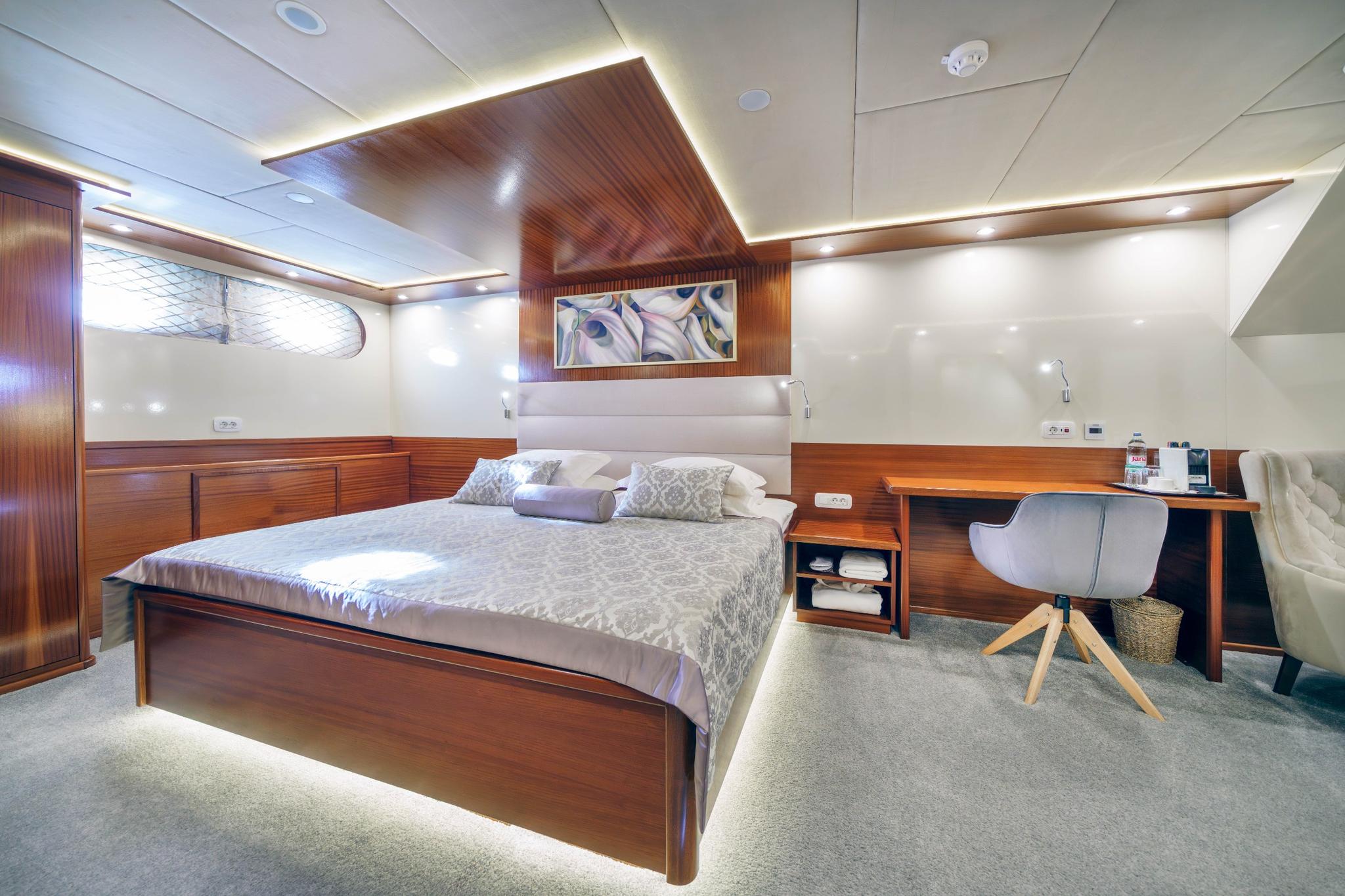 yacht cabin interior with wooden double bed, desk workspace, and white upholstered headboard