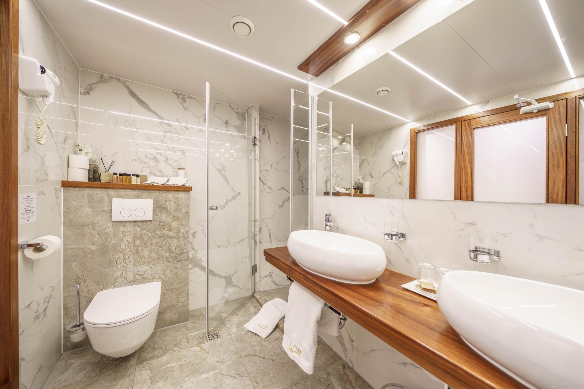 luxury yacht bathroom with white marble walls, wooden vanity counter, oval vessel sink and glass shower