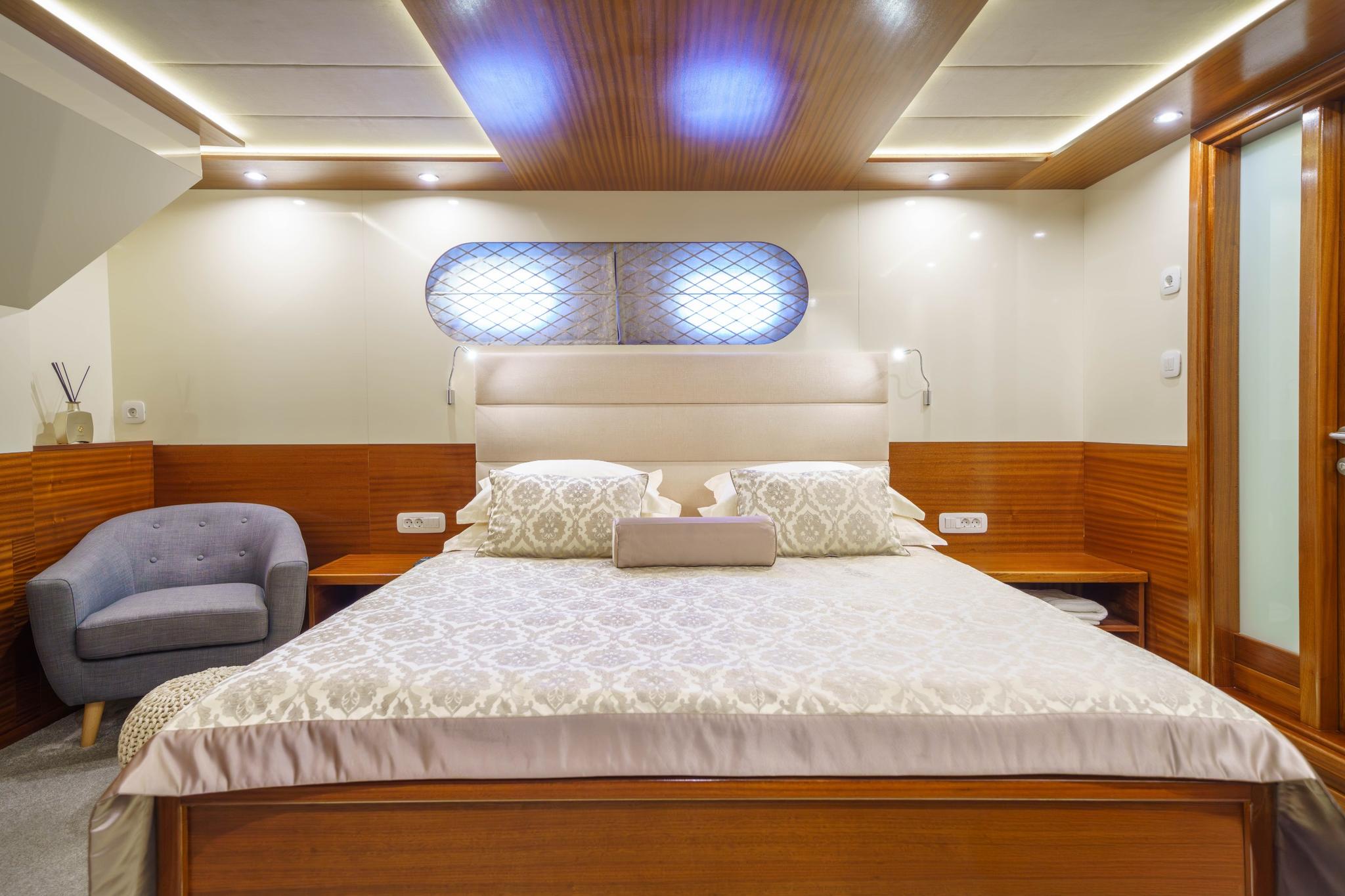 yacht cabin interior with double bed, white leather headboard, wooden paneling and gray armchair