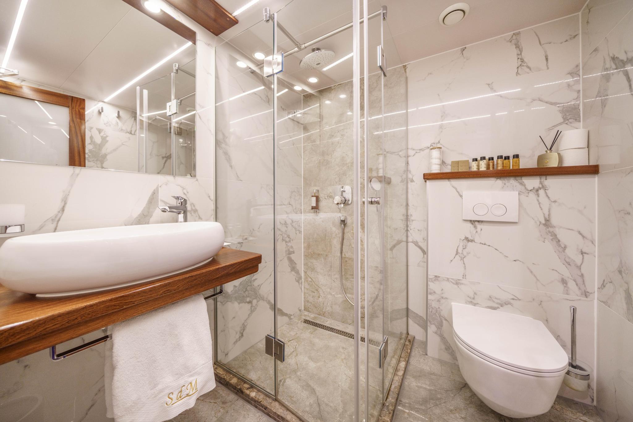 luxury yacht bathroom featuring marble walls, glass shower enclosure, oval basin and wall-mounted toilet