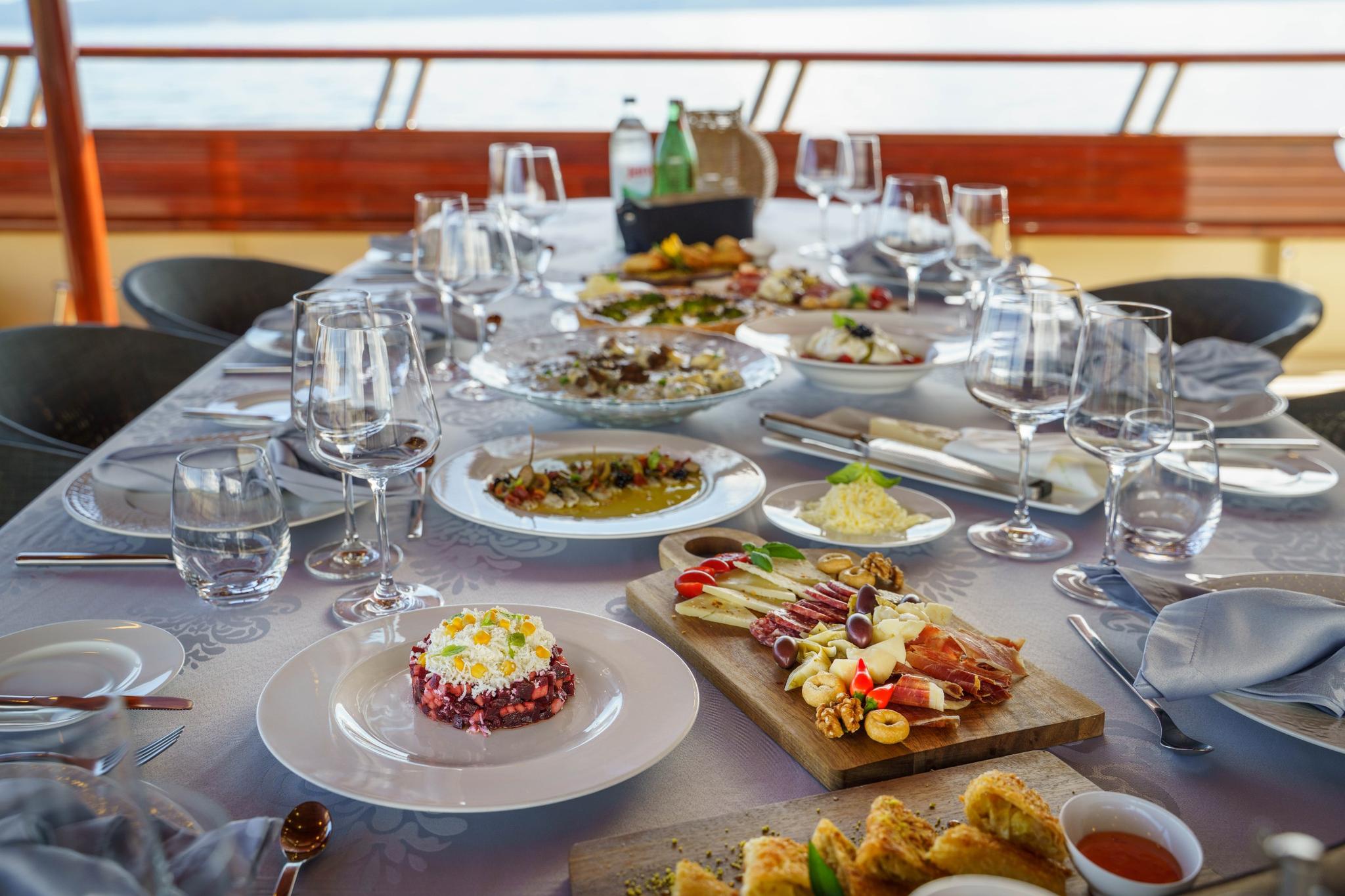 yacht dining table with charcuterie board, tartar dish, wine glasses and gourmet meal setup