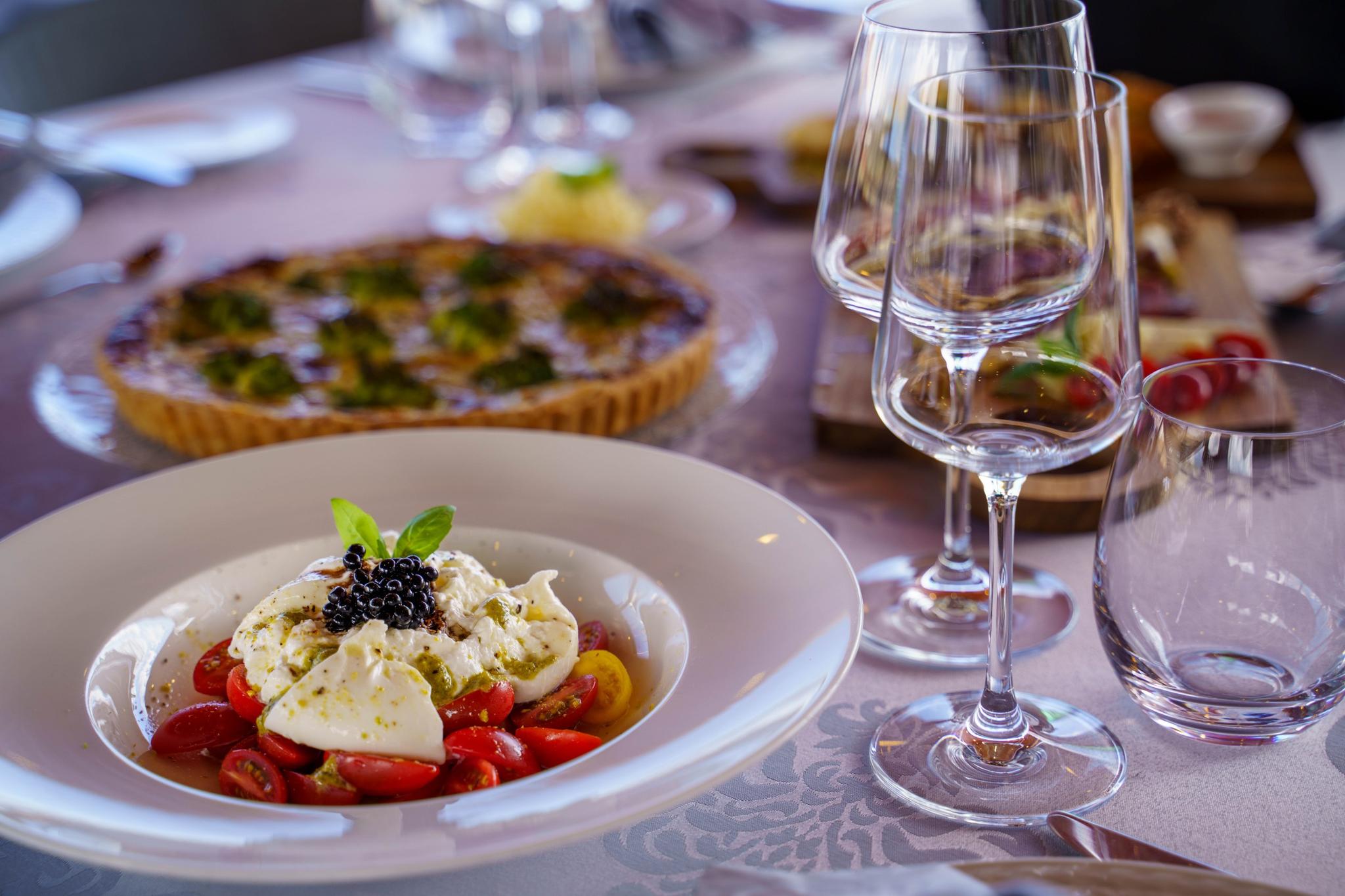 elegant dining setup with burrata salad, cherry tomatoes, caviar and wine glasses