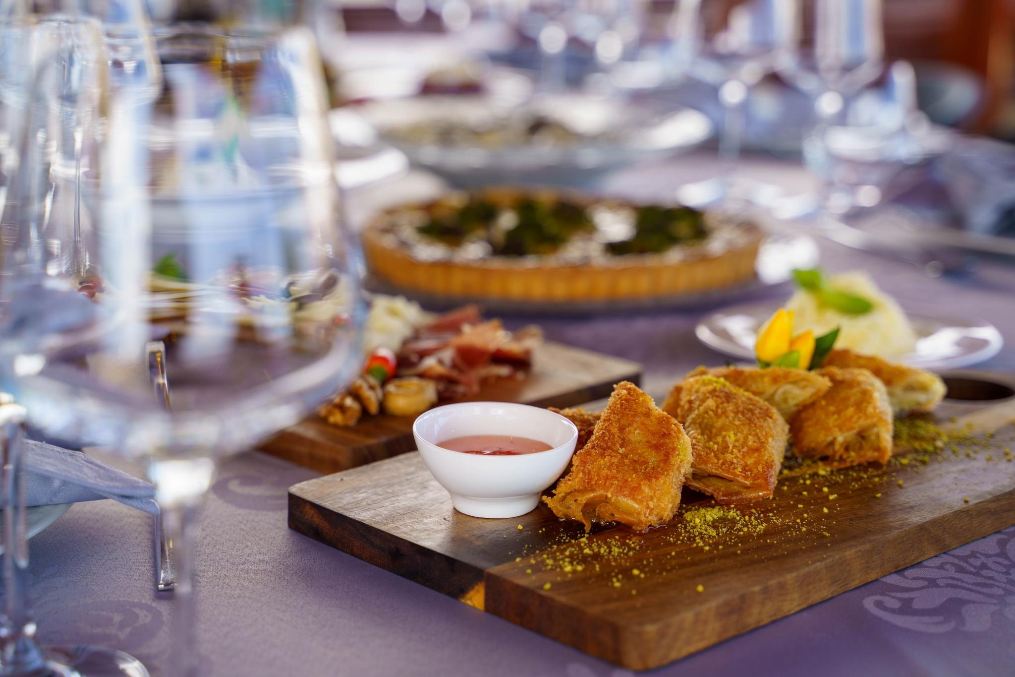 Golden baklava pastries with pistachio garnish and red syrup served on wooden cutting board