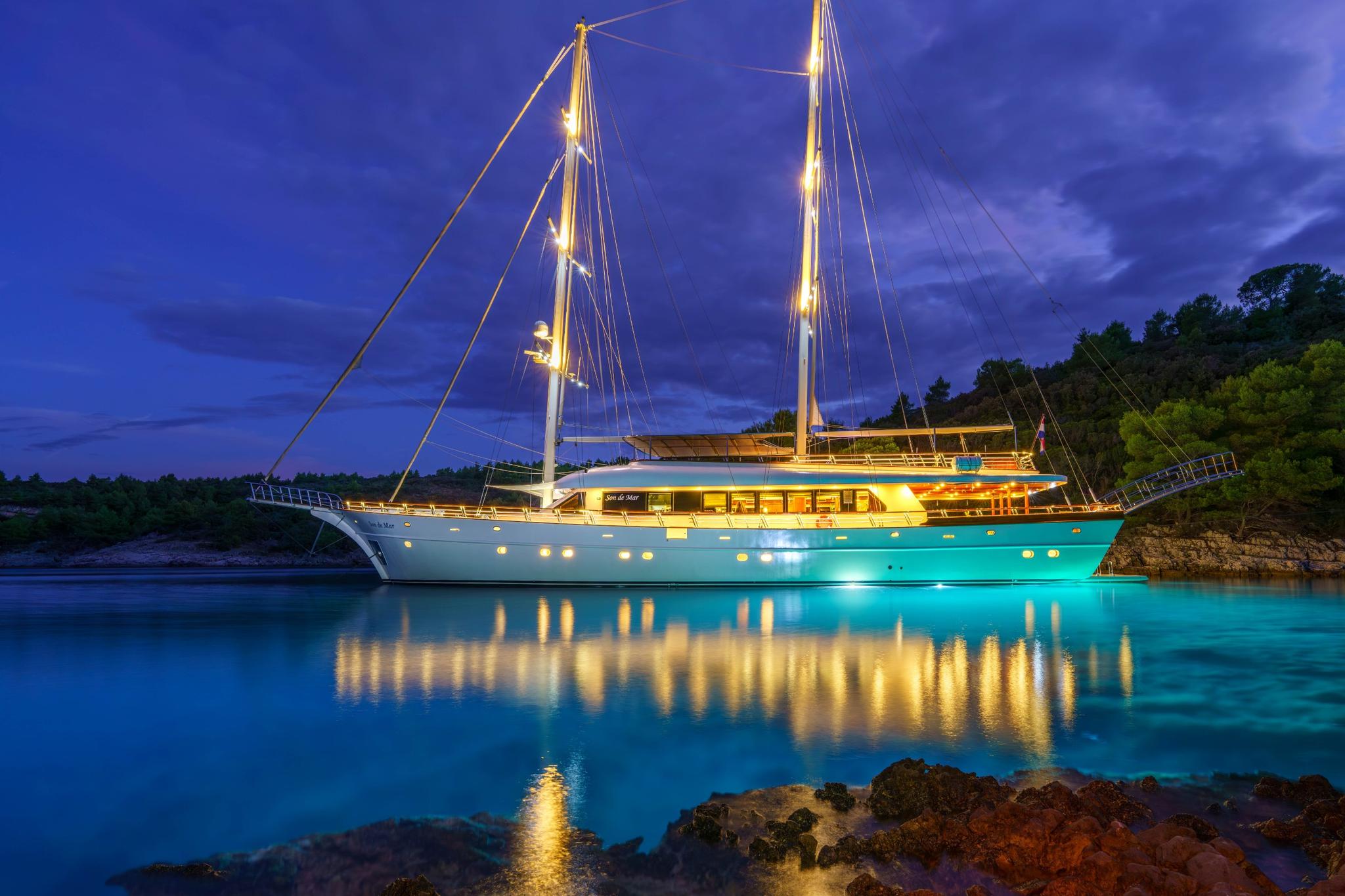 Traditional wooden gulet with two masts anchored in calm turquoise bay at dusk