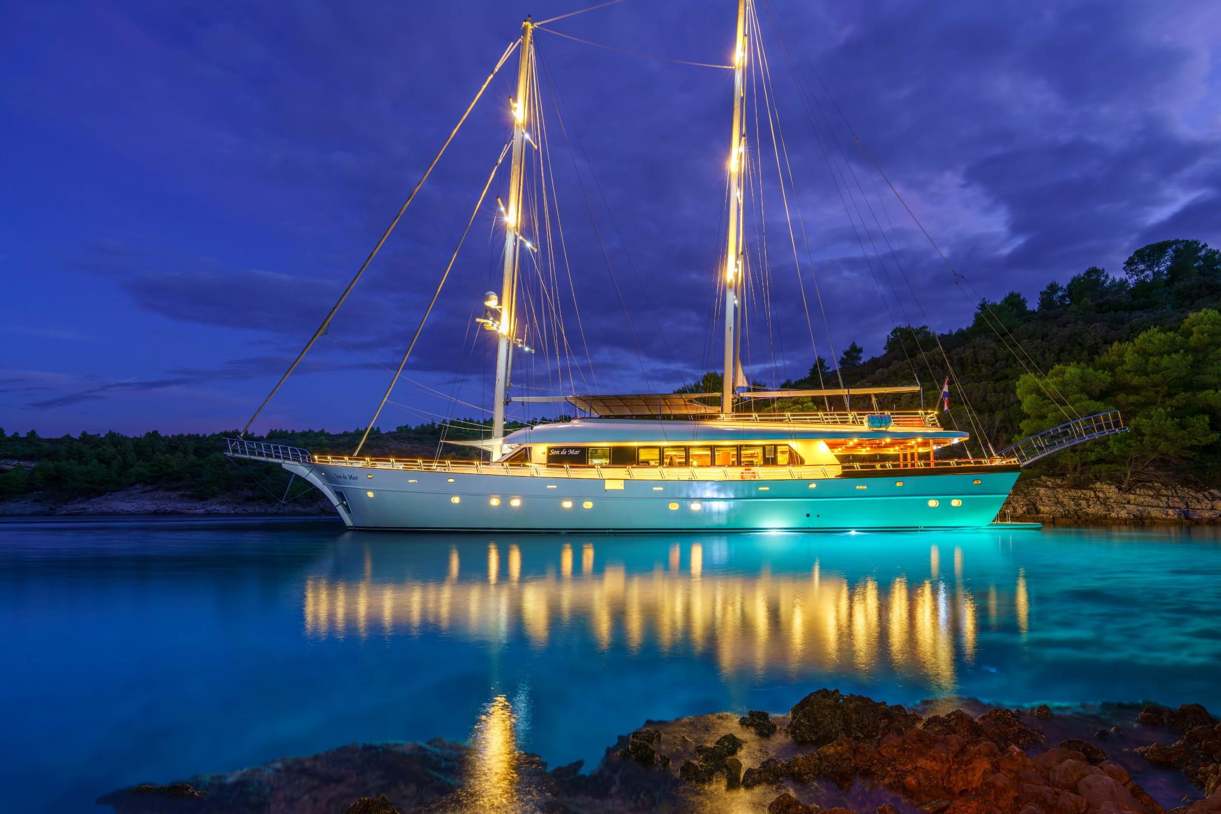 Traditional wooden gulet with two masts anchored in calm turquoise bay at dusk