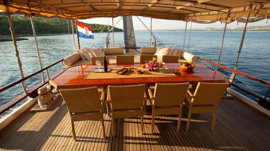 Gulet yacht aft deck dining table with Croatian flag and coastal views