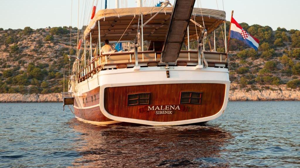 Wooden gulet Malena stern view with Croatian flag anchored near rocky coastline